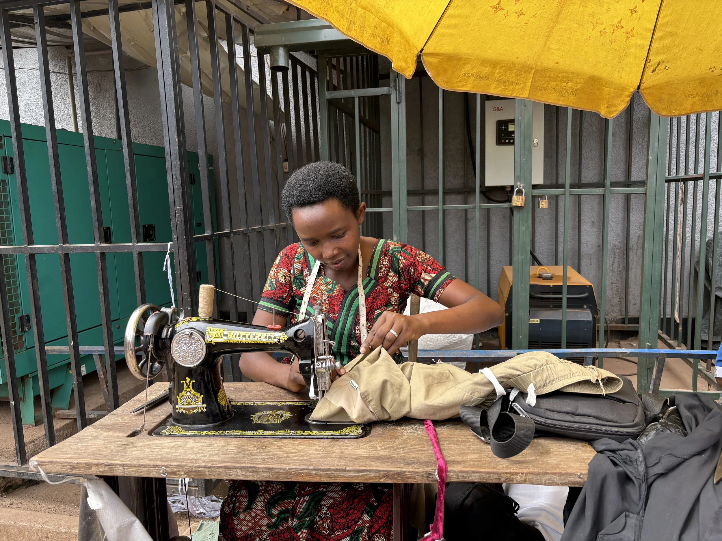 A woman sewing with a vintage Singer sewing machine outdoors under a yellow umbrella.