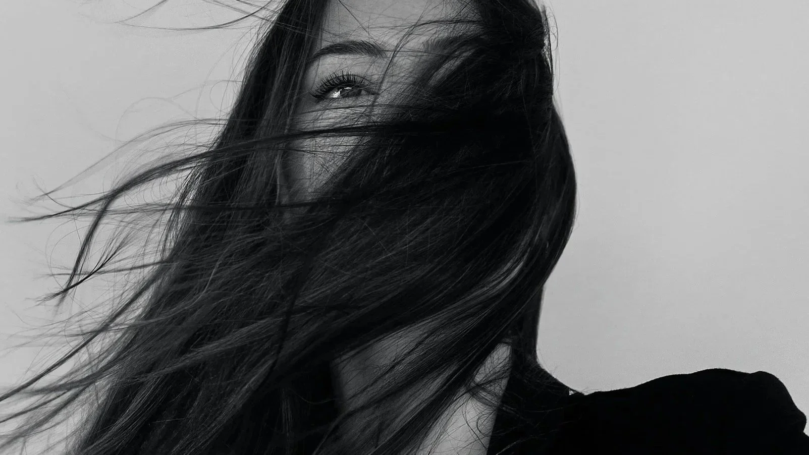 Black and white photograph of a woman with long hair, partially covering her face, with one visible eye looking at the camera.
