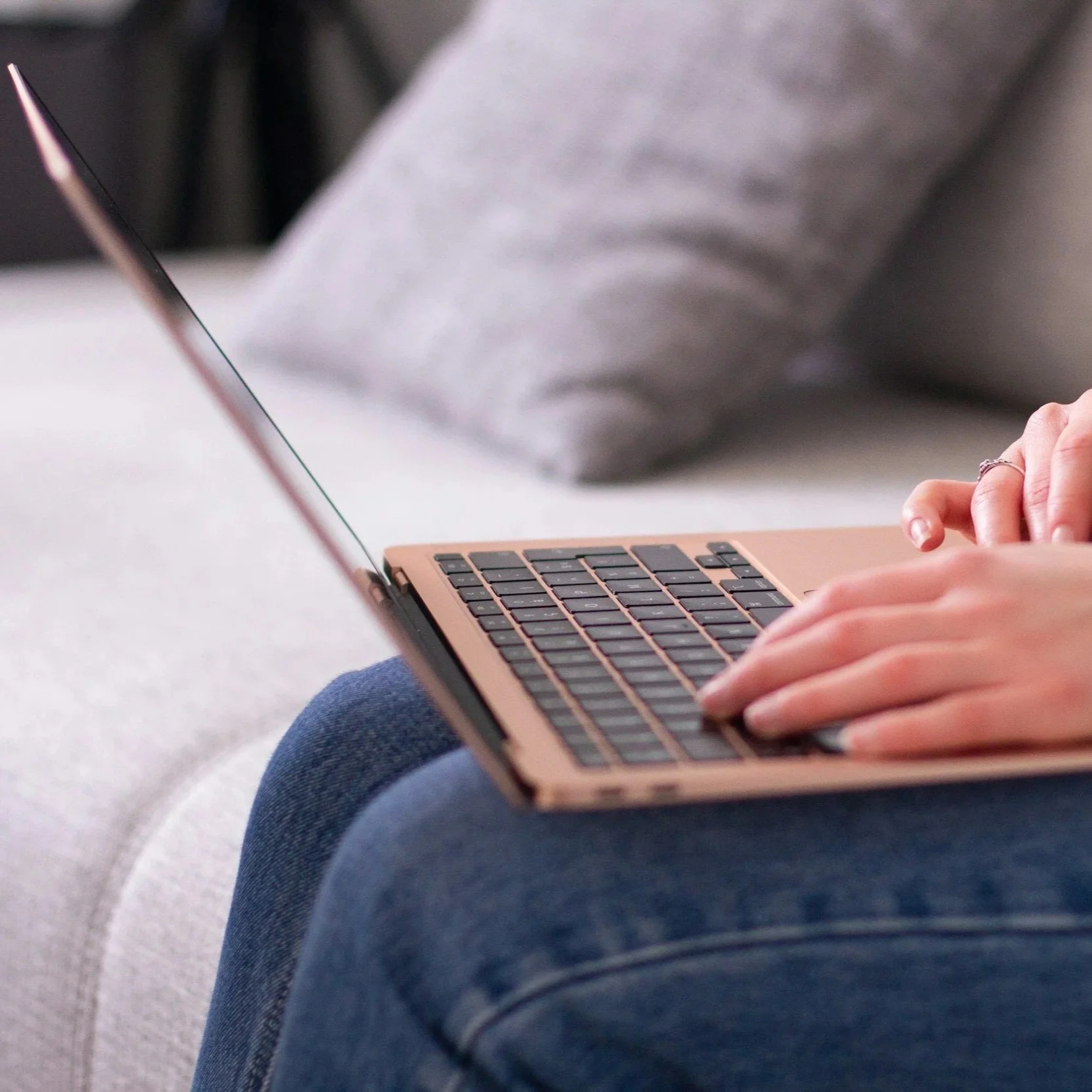 Person using a laptop on a couch, focusing on hands typing on the keyboard.