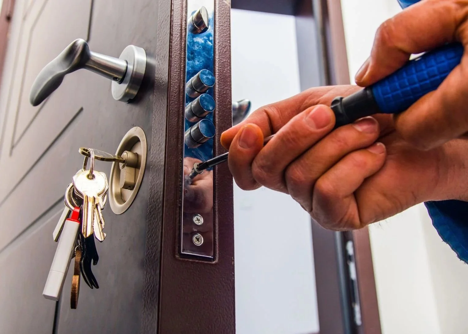 Une personne déverrouille une porte avec un tournevis, porte équipée de plusieurs serrures et clés