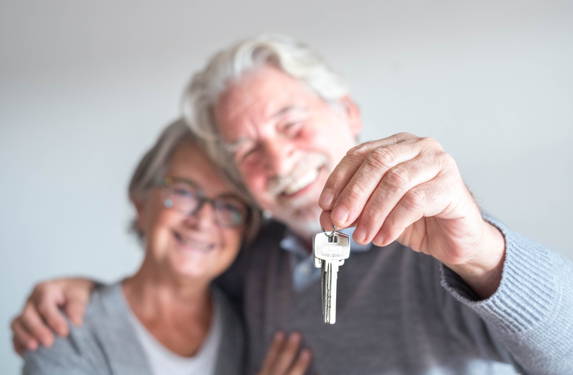 Un couple âgé souriant, tenant une clé de maison, symbolisant une sécurisation de leur domicile.