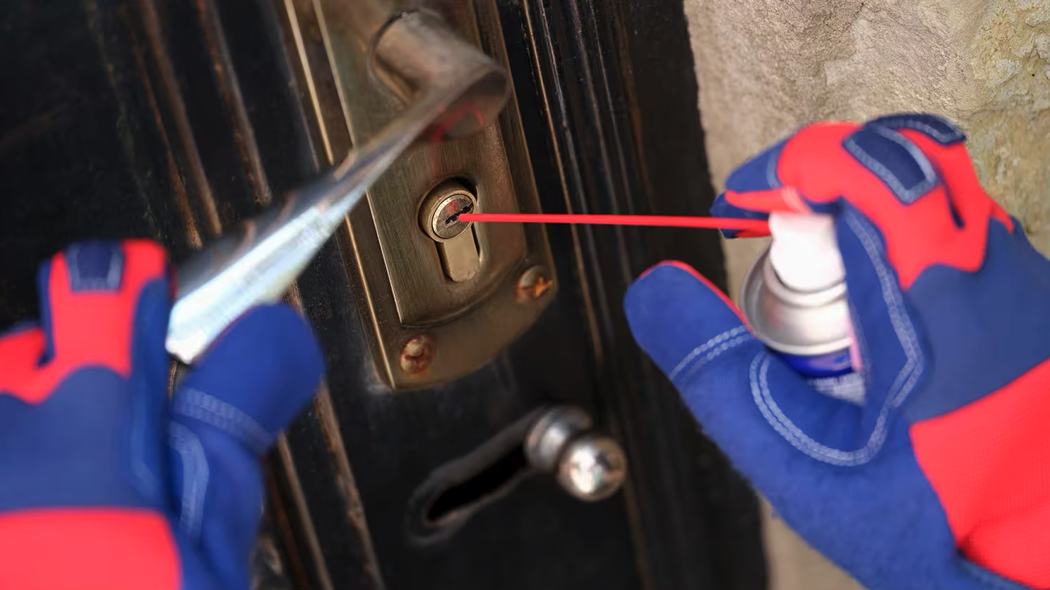 Mains en gants de protection pulvérisant du dégrippant sur une serrure de porte.