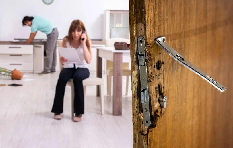 Une porte en bois avec une serrure cassée et la poignée enlevée, dans une pièce où une femme assise appel son serrurier de confiance et son assurance suite à un cambriolage