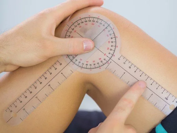 A woman sitting upright on an examination table with a pillow behind her back, receiving physiotherapy from a male therapist who is pressing on her lower back. They are in a clinical setting with a sign that reads "Cite Physiotherapy" on the wall.