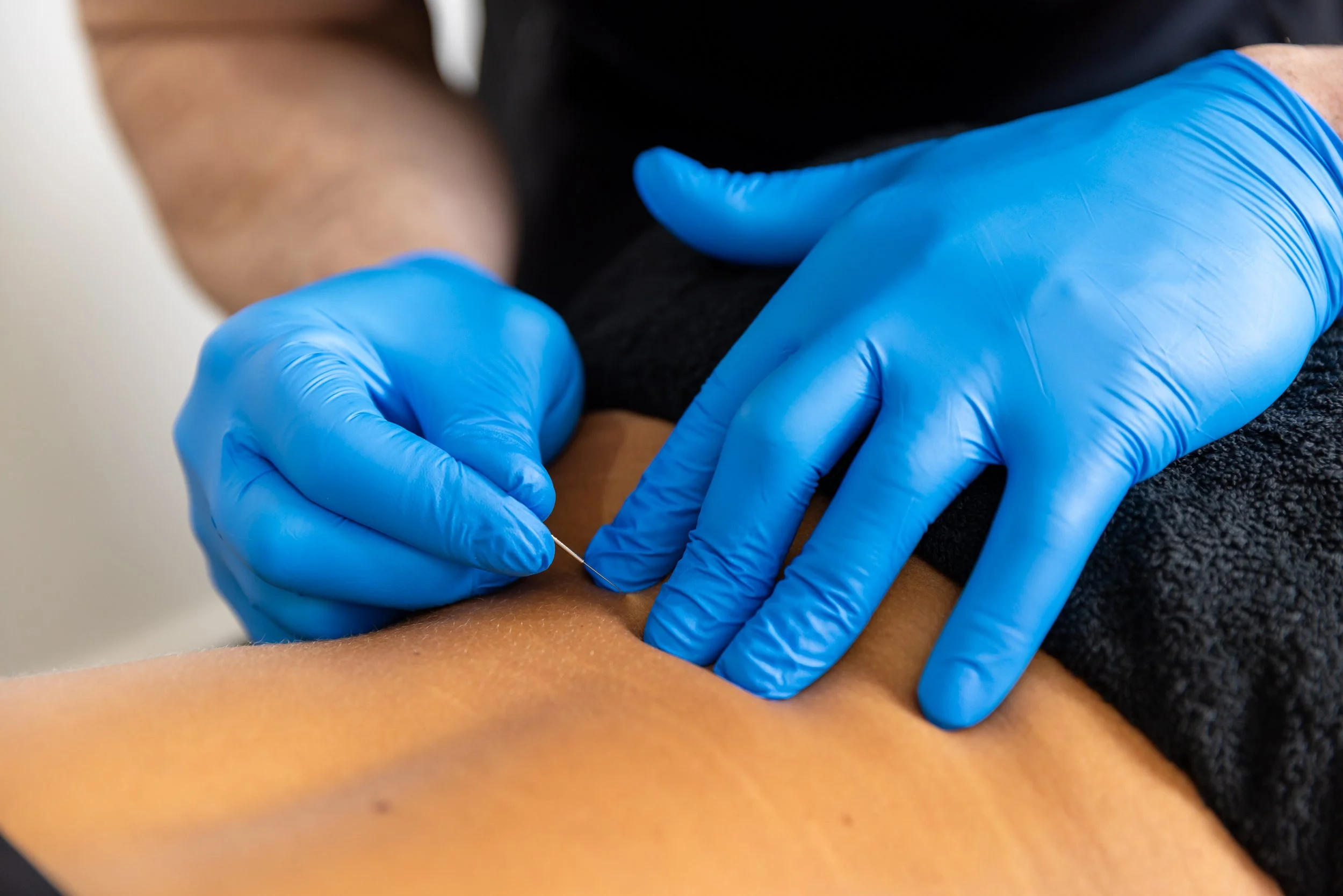 A person wearing blue gloves administering an injection into another person's arm.