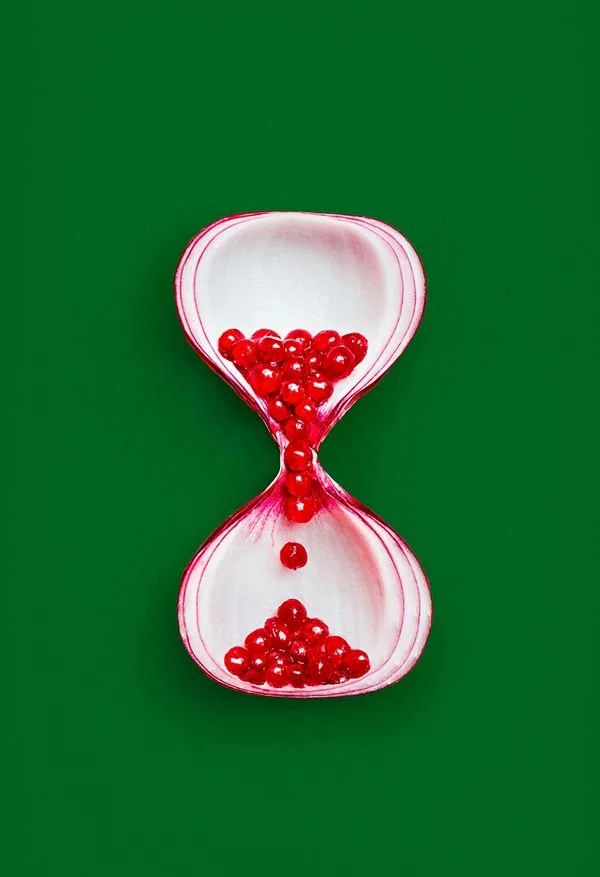 An hourglass-shaped container with red beads inside, set against a green background.