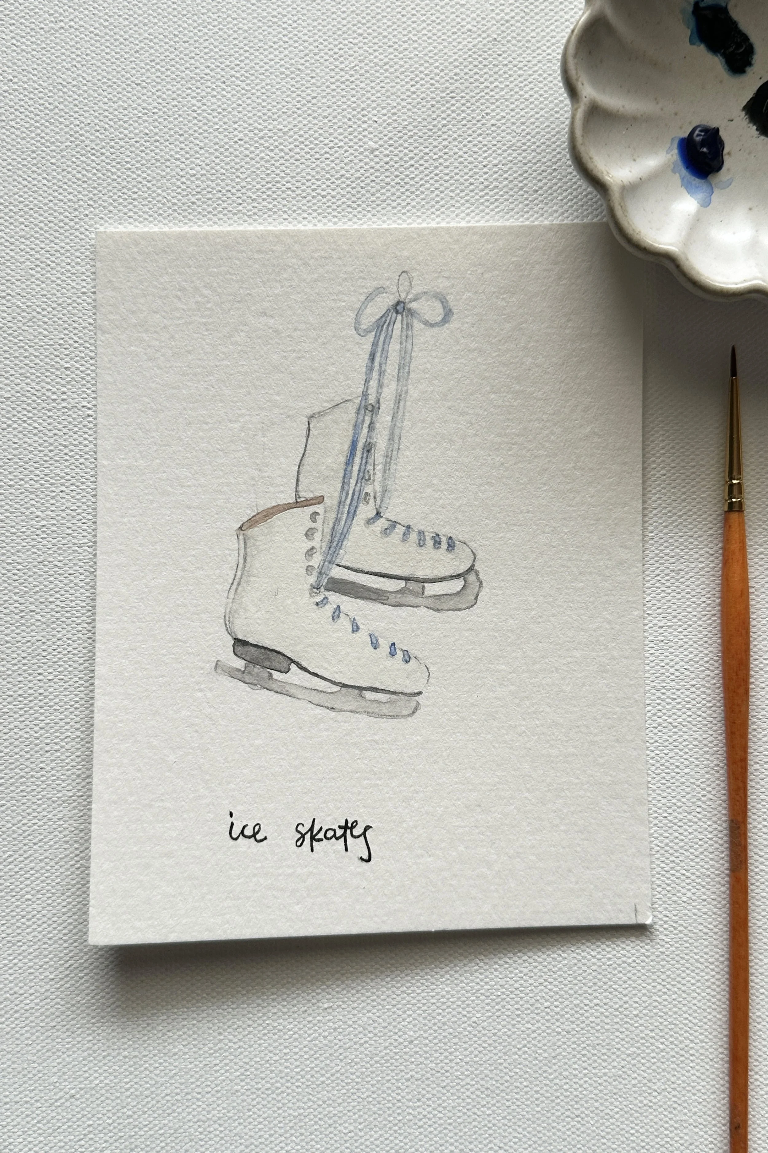 A soft watercolor painting of ice skates, part of the January Winter Wonderland theme.