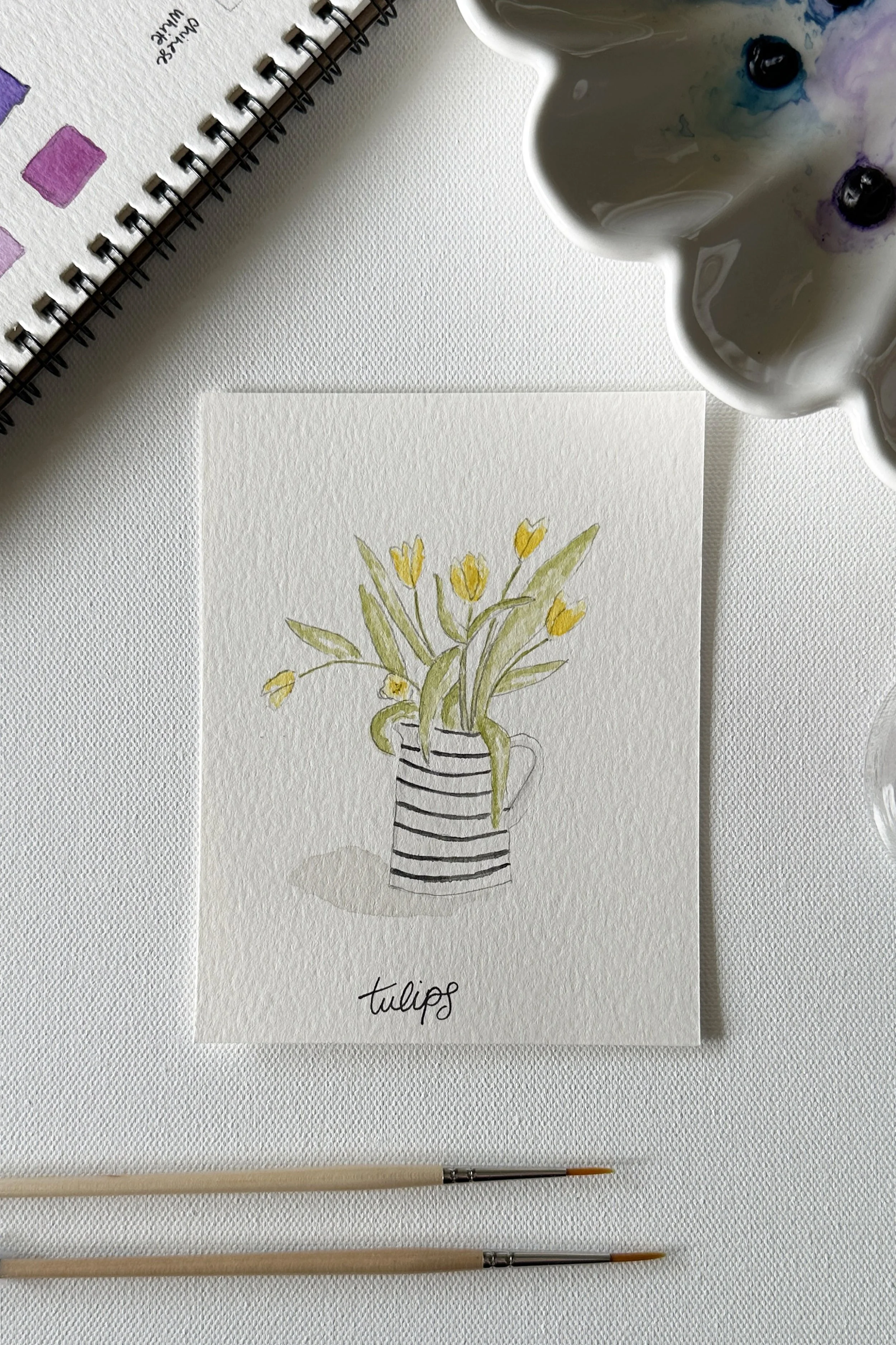 A watercolor of yellow tulips in a striped jug, part of the May flowers theme.