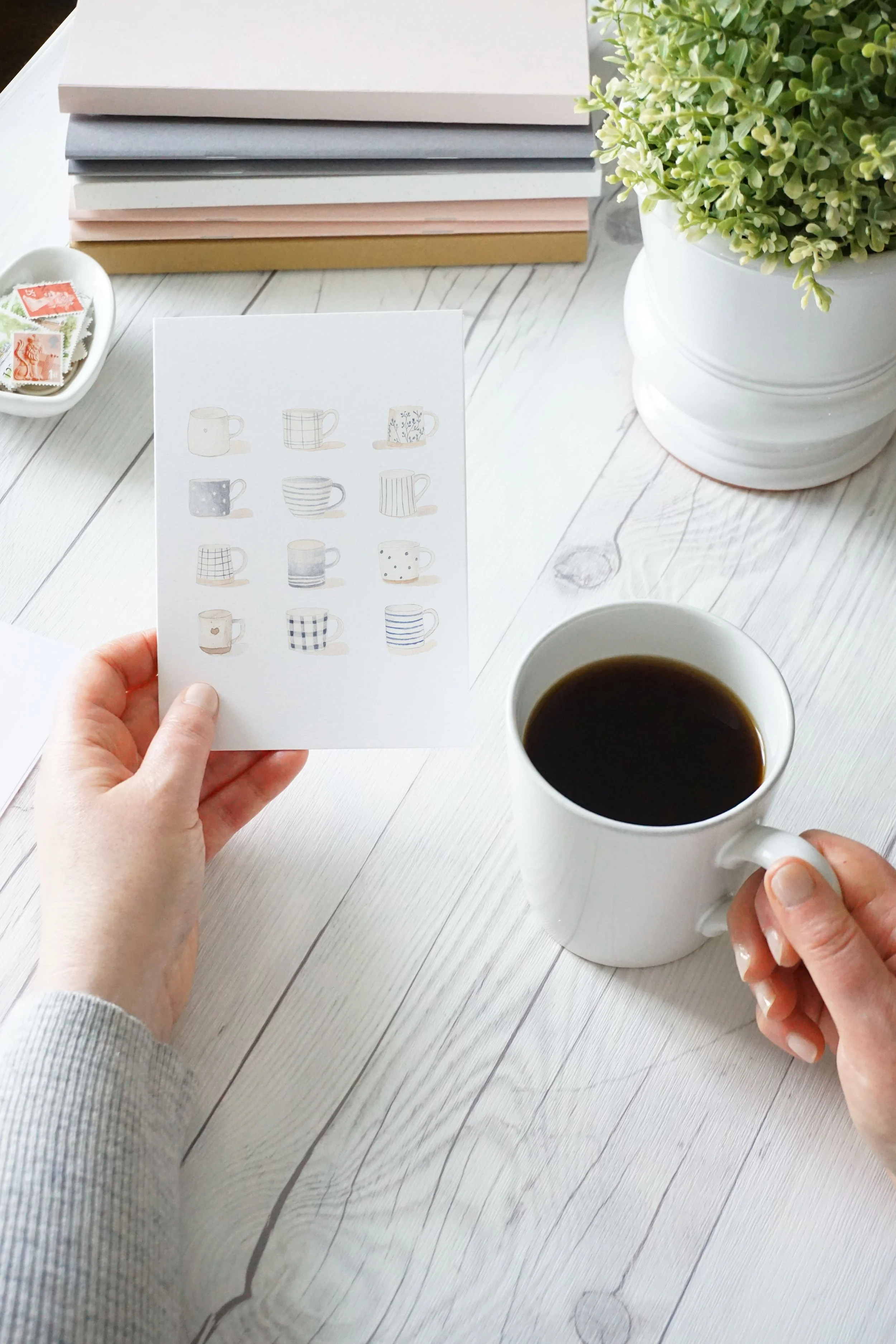Hand holding a watercolor greeting card with a cup of coffee.