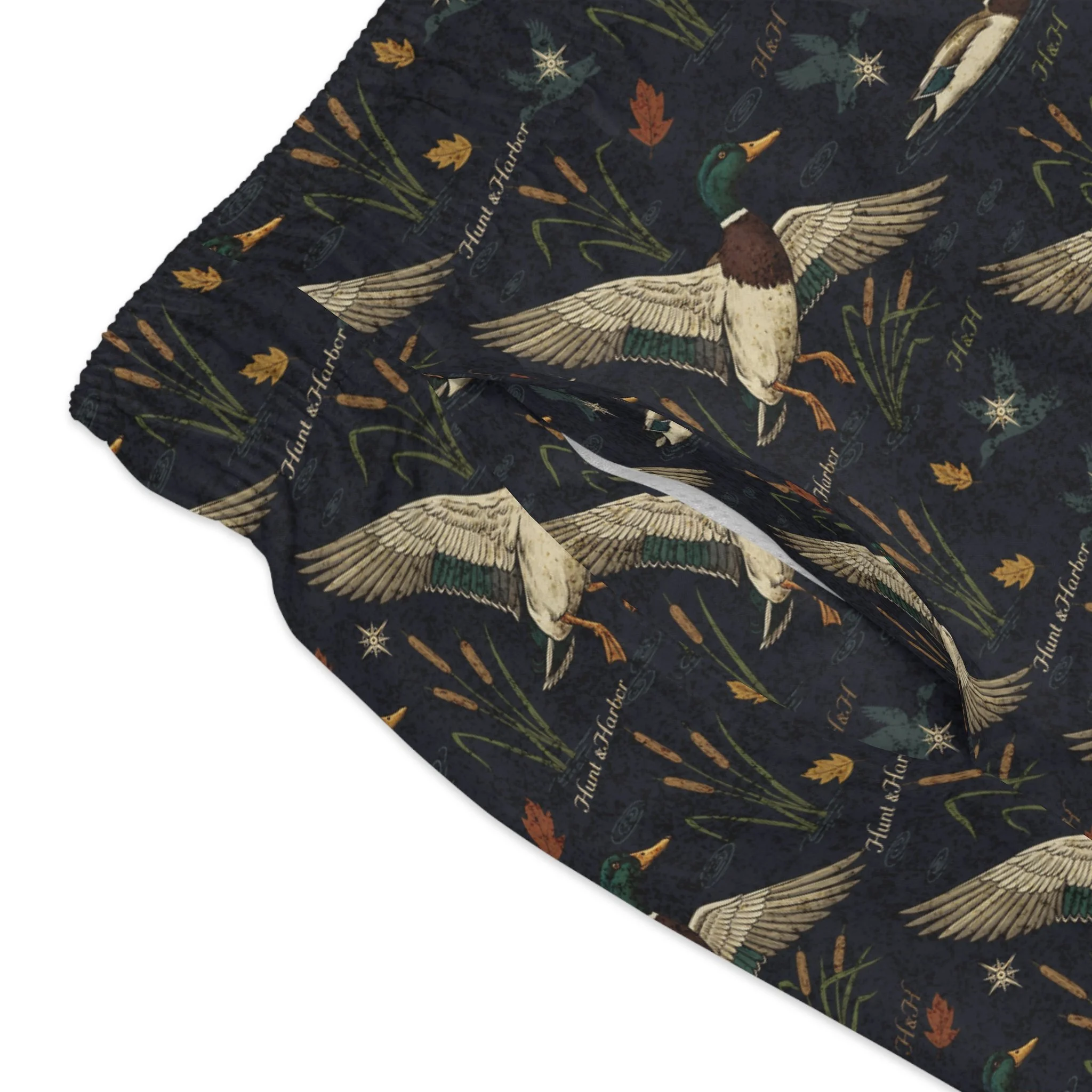 Close up of vintage mallard drake landing illustration with cattails and autumn leaves on Hunt and Harbor men's navy swim trunks