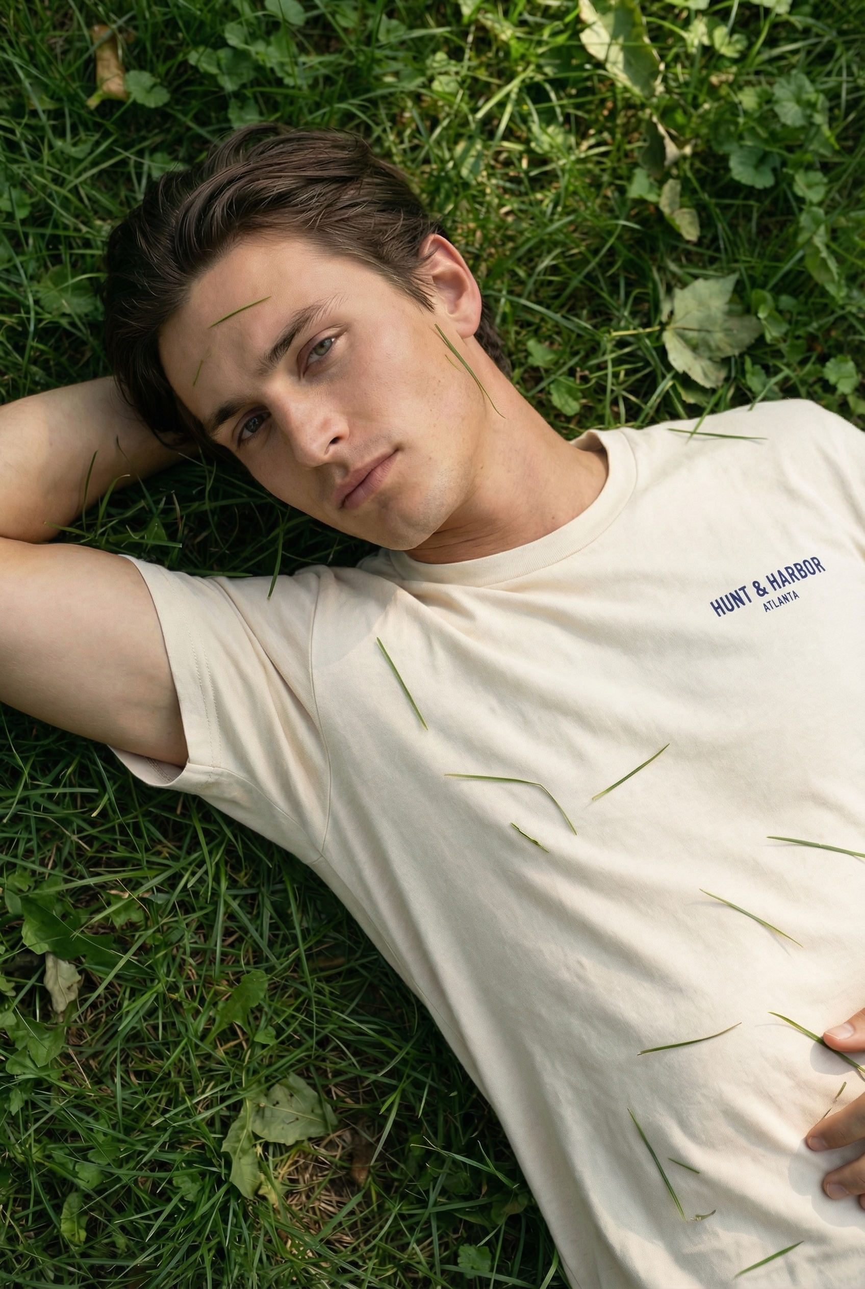 A young man walking on a wooden dock near a lake during sunset, wearing a gray quarter-zip sweatshirt and black pants.