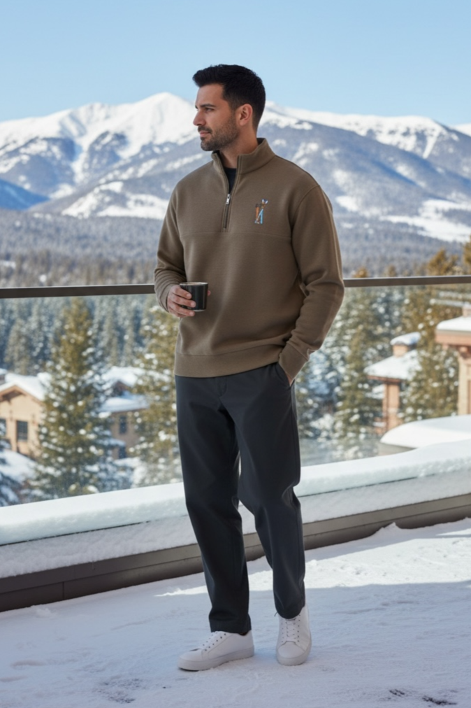 A young man walking on a wooden dock near a lake during sunset, wearing a gray quarter-zip sweatshirt and black pants.