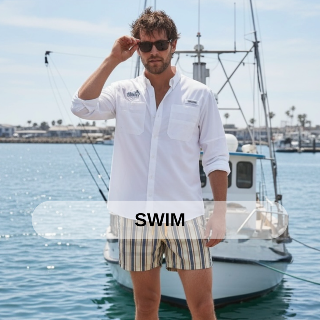 A man standing in front of a boat at the marina, wearing sunglasses, a white button-up shirt, and striped shorts.