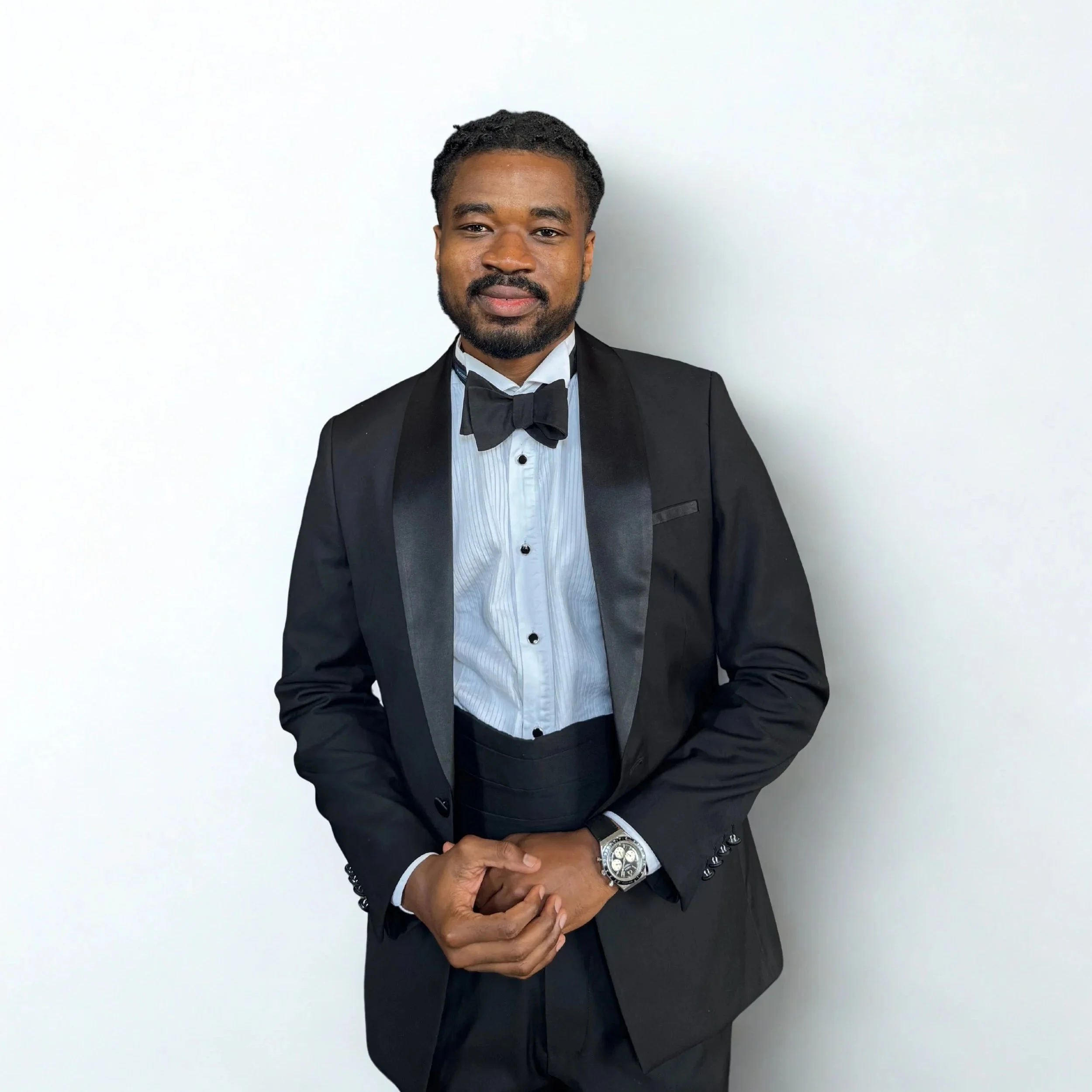 Man in tuxedo with bow tie standing against plain white wall