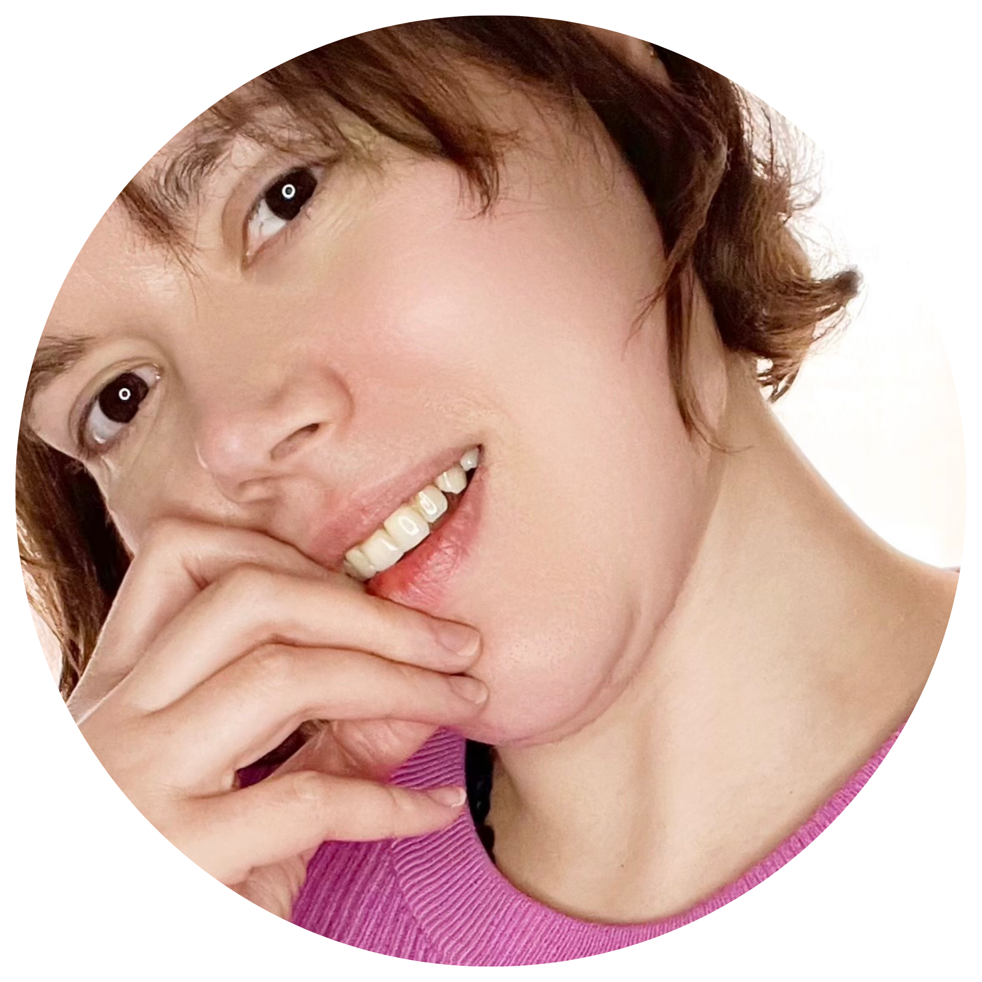 Jeune femme avec des cheveux bruns courts, souriante, portant un pull violet, tenant sa main devant sa bouche, regardant en face.