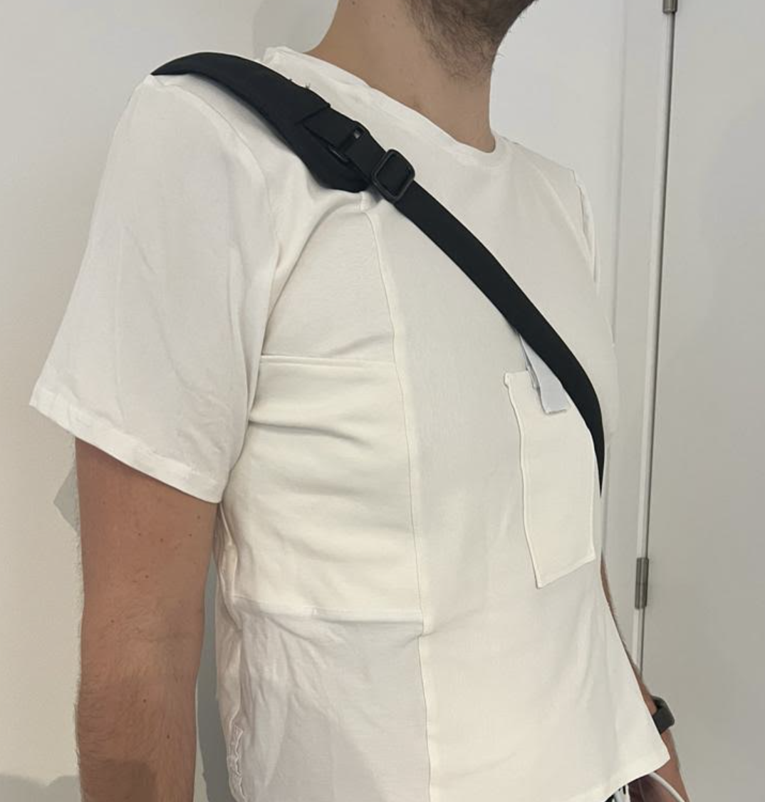 Un homme en t-shirt blanc portant un sac à bandoulière noir.
