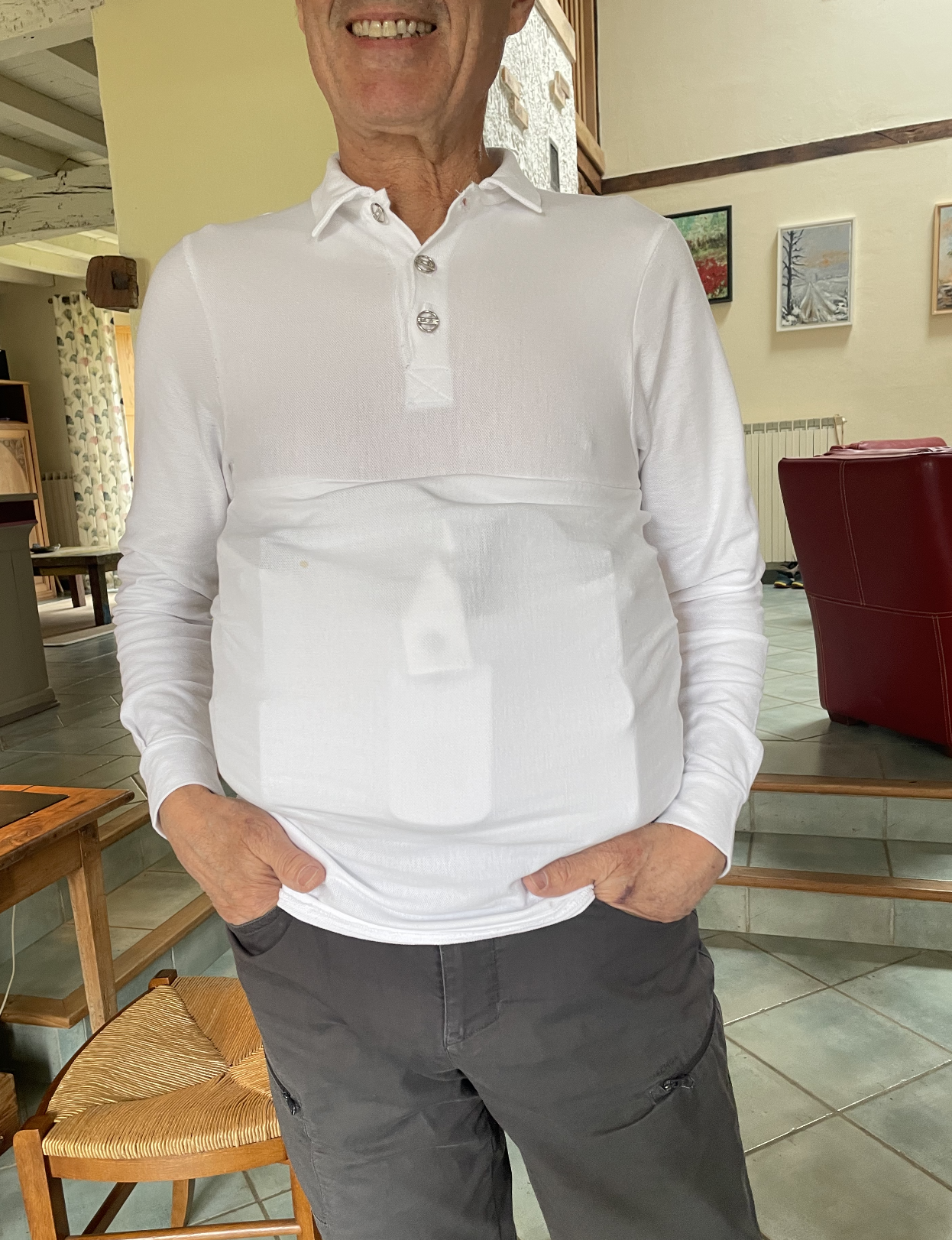 Un homme portant un polo blanc à col et une veste noire, debout dans un intérieur avec des œuvres d'art accrochées au mur.