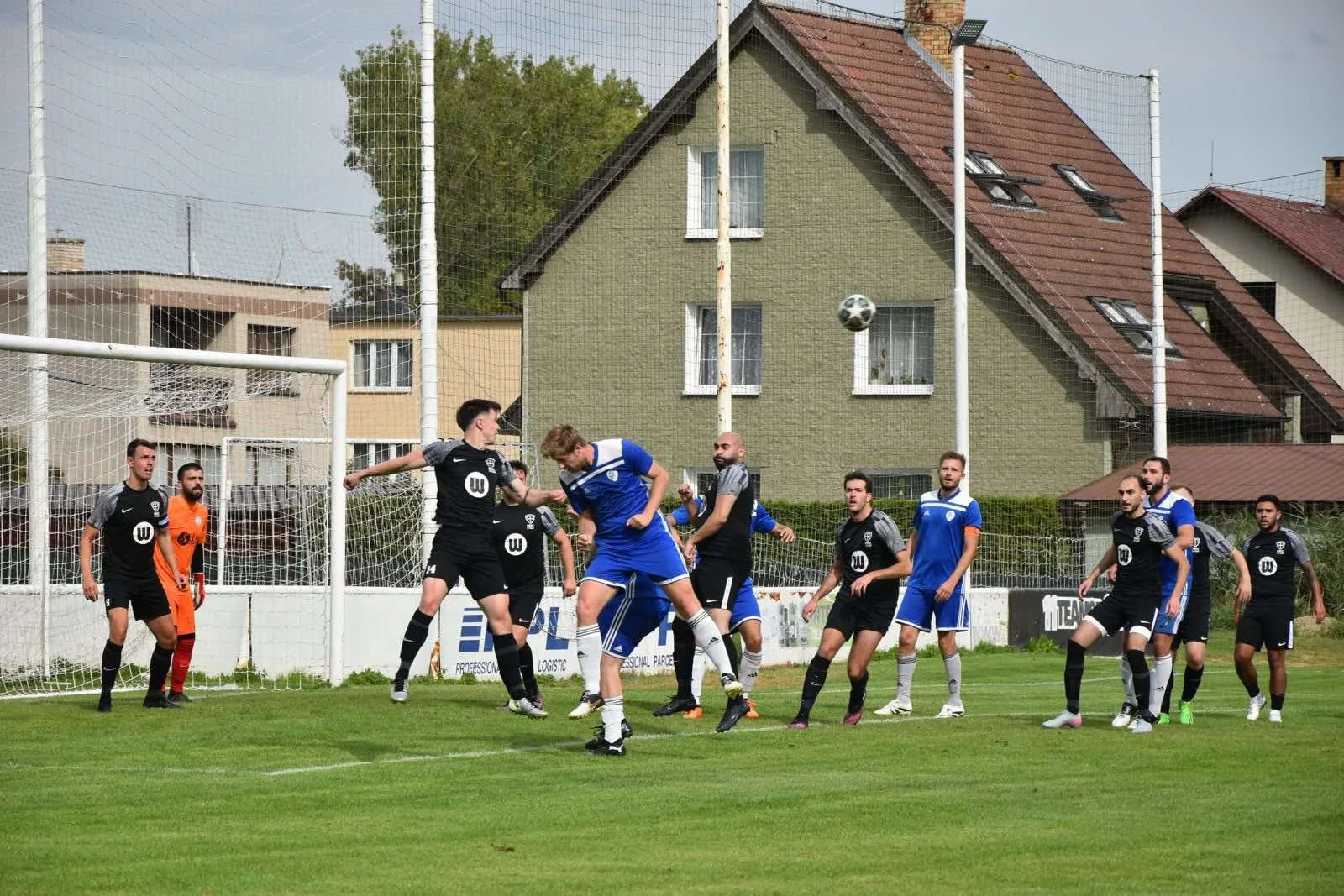 Soccer players in black and blue jerseys competing in a game near the goal, with one player heading the ball as several teammates watch on.