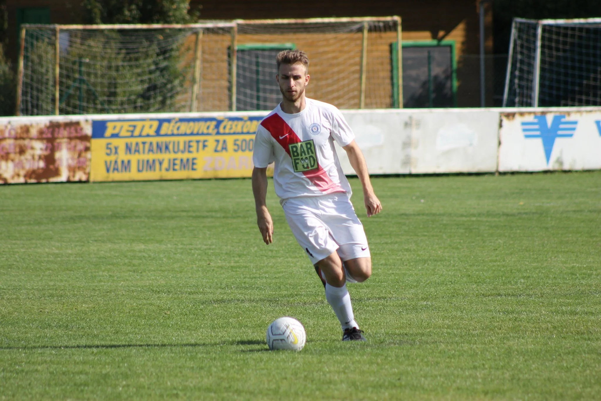 A soccer player in a white uniform with red and black accents dribbling a soccer ball on a green field.