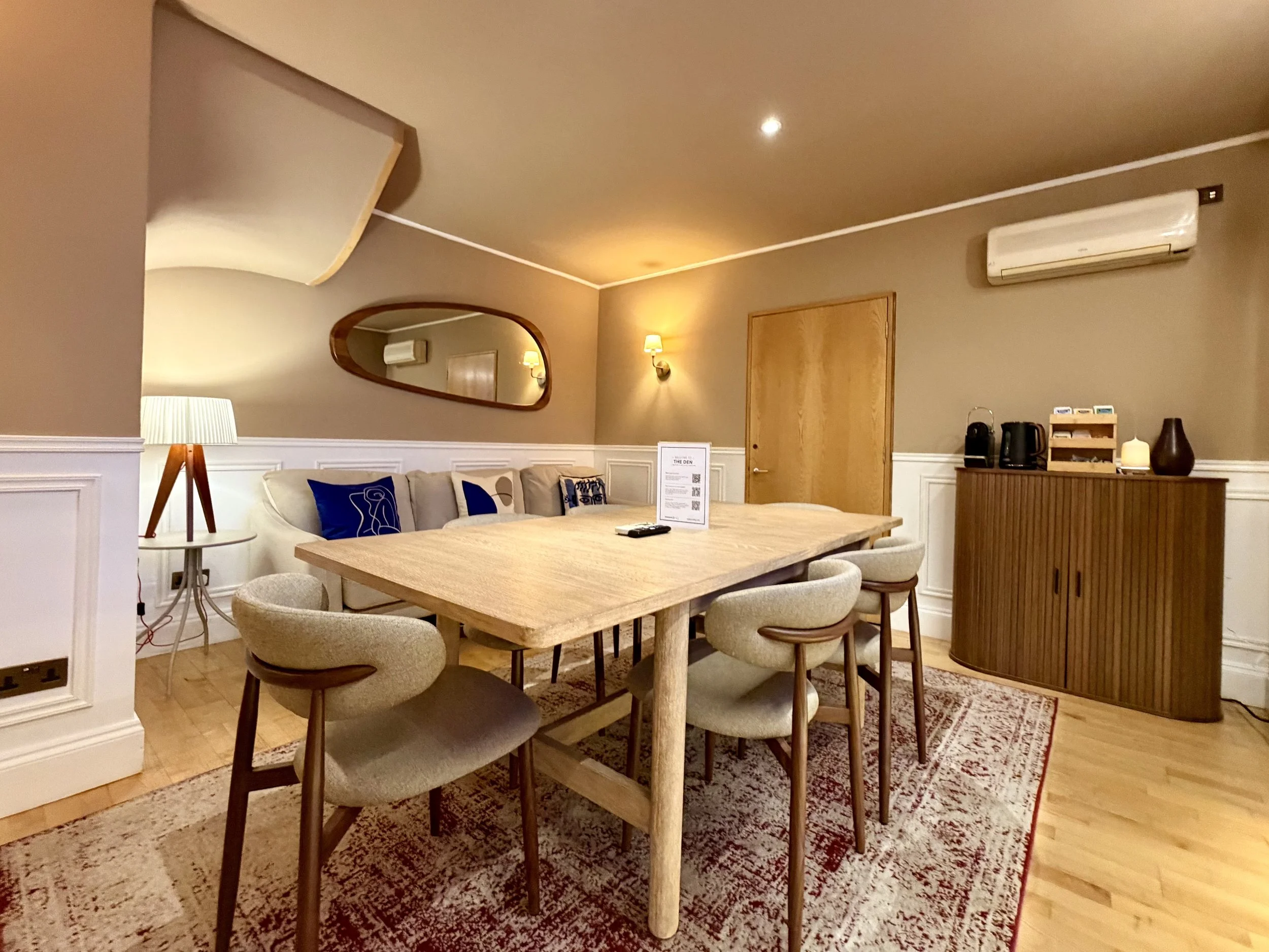 A boardroom with brown overtones, featuring a large oak table with chairs all around, a mirror attached to the wall and a generous sofa.