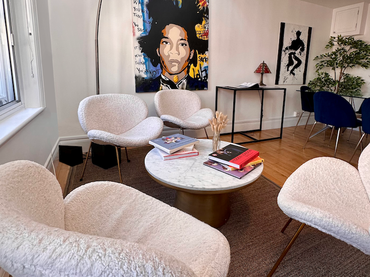 Four white, fluffy chairs surround a marble coffee table on a rug, with artwork and white walls creating a light, bright space.