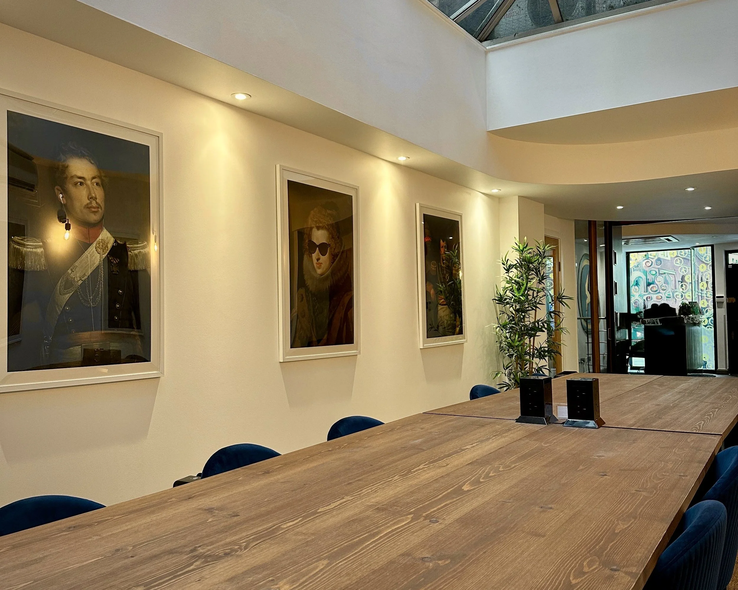 A large meeting room featuring a conservatory-style ceiling, with bright white walls and a large wooden-style table surrounded by blue chairs.