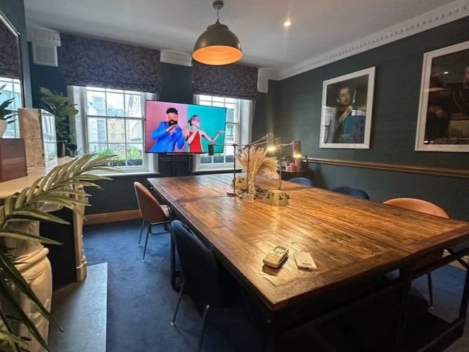 A meeting room in Soho, London with a big oak boardroom table with blue and orange chairs and big windows looking over Wardour Street