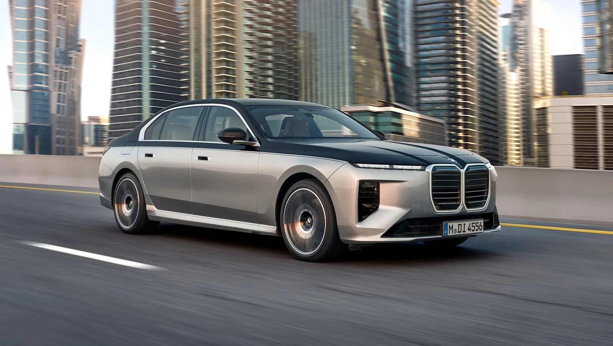 A sleek modern electric car driving on a city highway with tall glass skyscrapers in the background.
