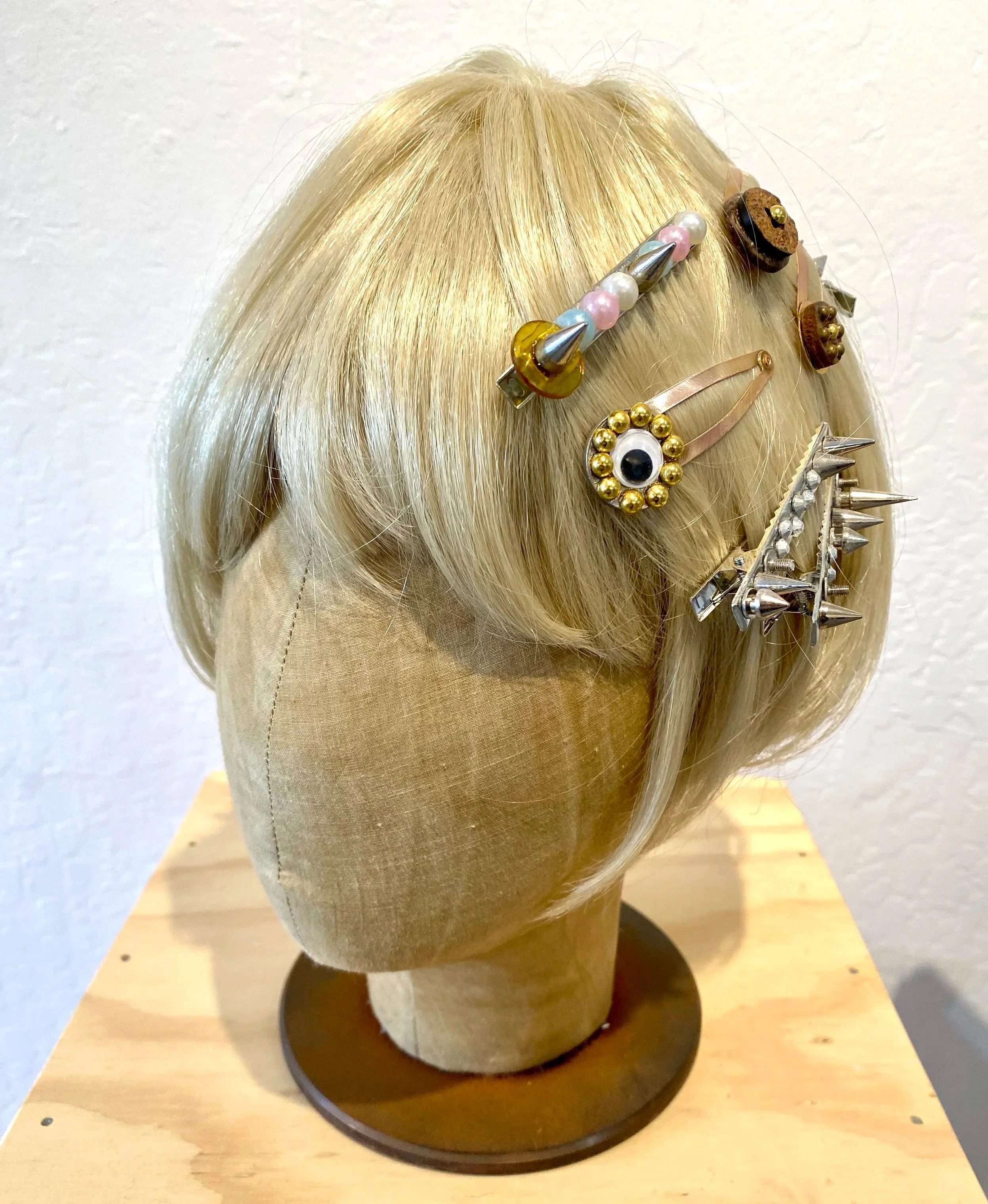 Blonde mannequin head with various decorative hair clips and pins in the hair.