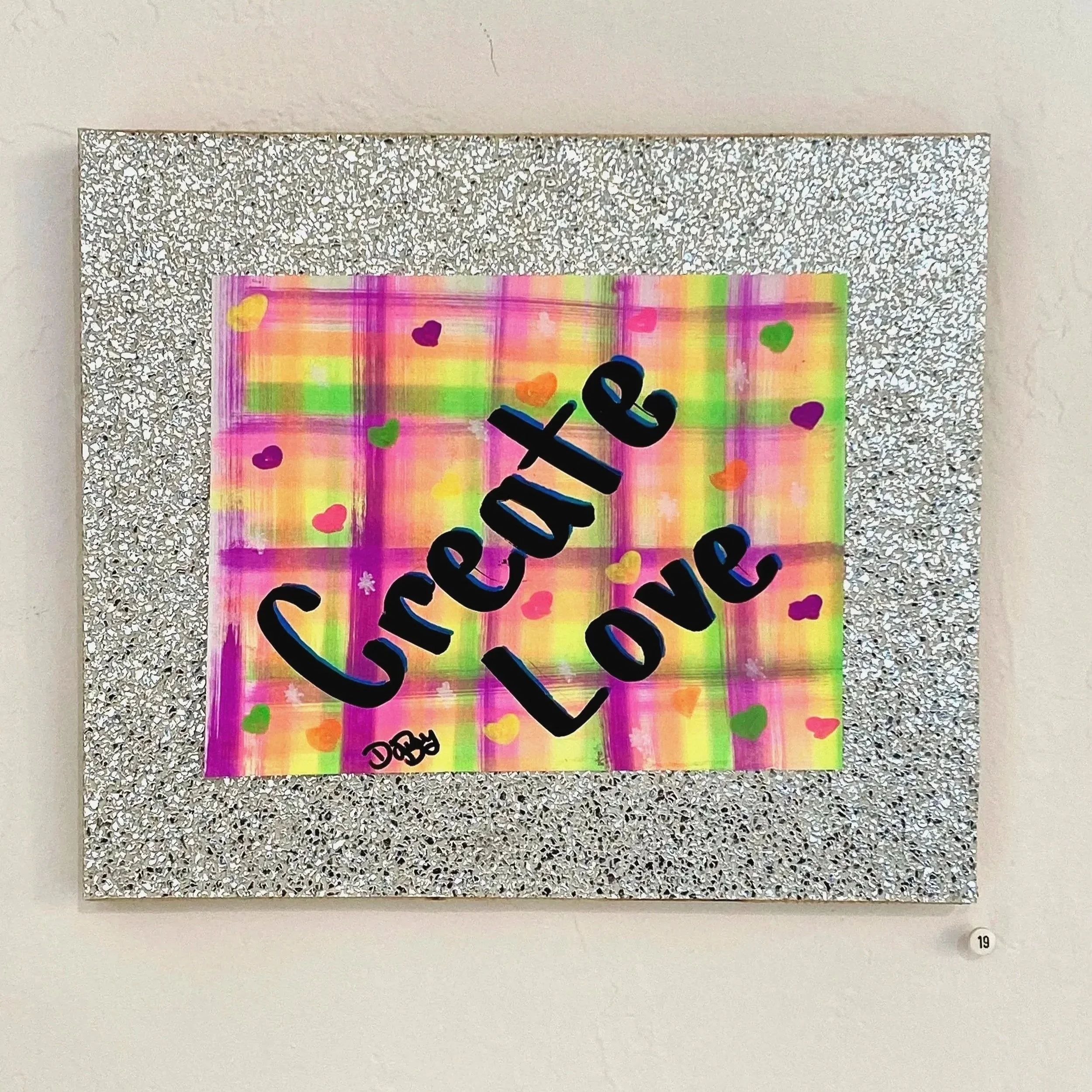 Colorful artwork with the phrase 'Create Love' written in large black letters, featuring a multicolored background with hearts and stars, surrounded by a silver glittery frame.