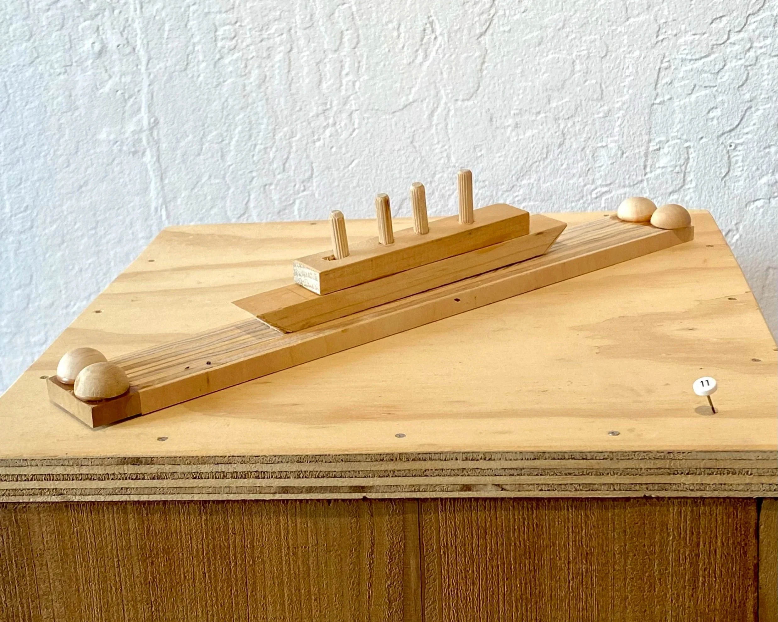 A wooden model of a ship on a wooden base, with small wooden balls and a plaque with the number 17.