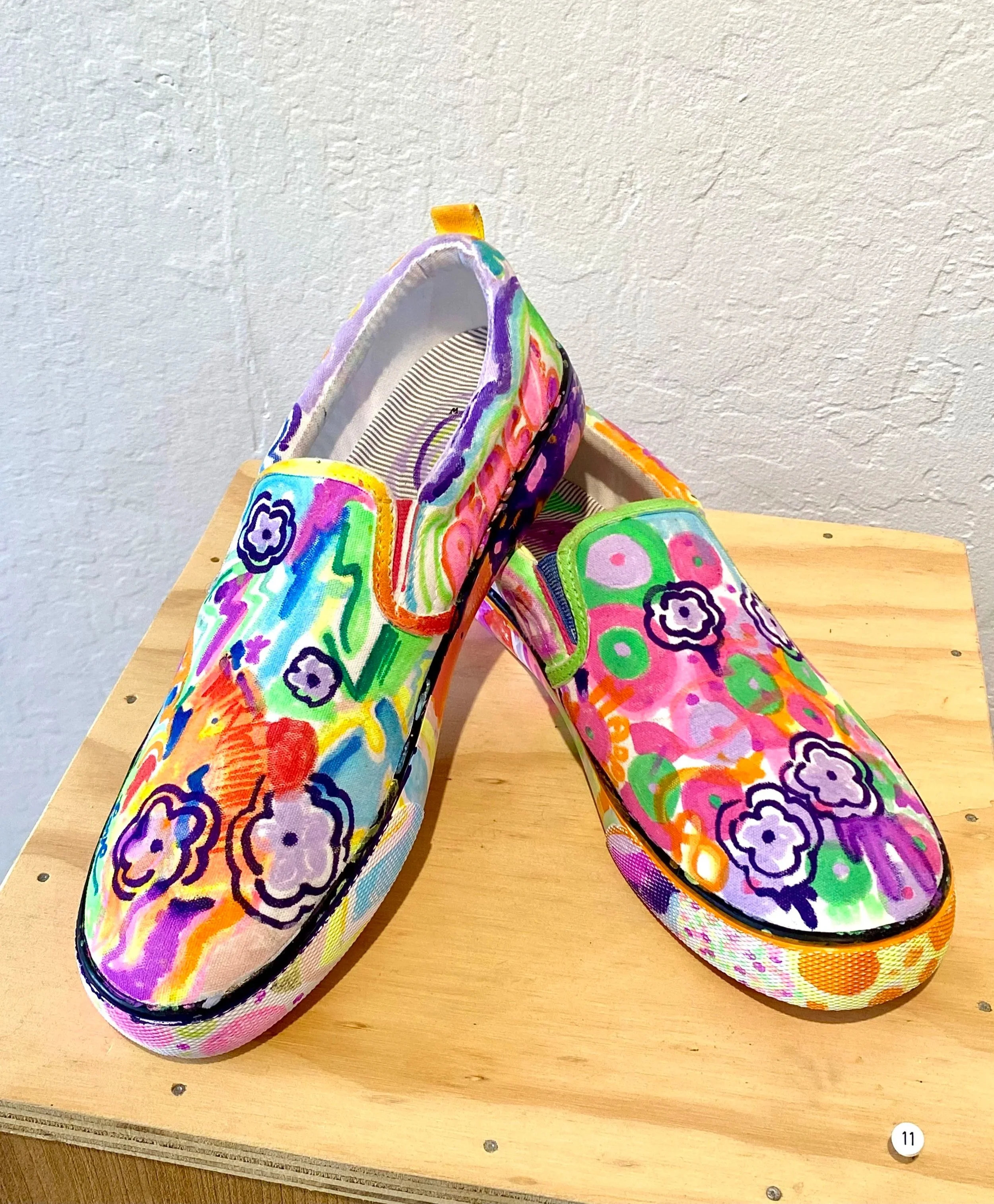 Colorful slip-on shoes with floral and abstract patterns on a wooden surface.
