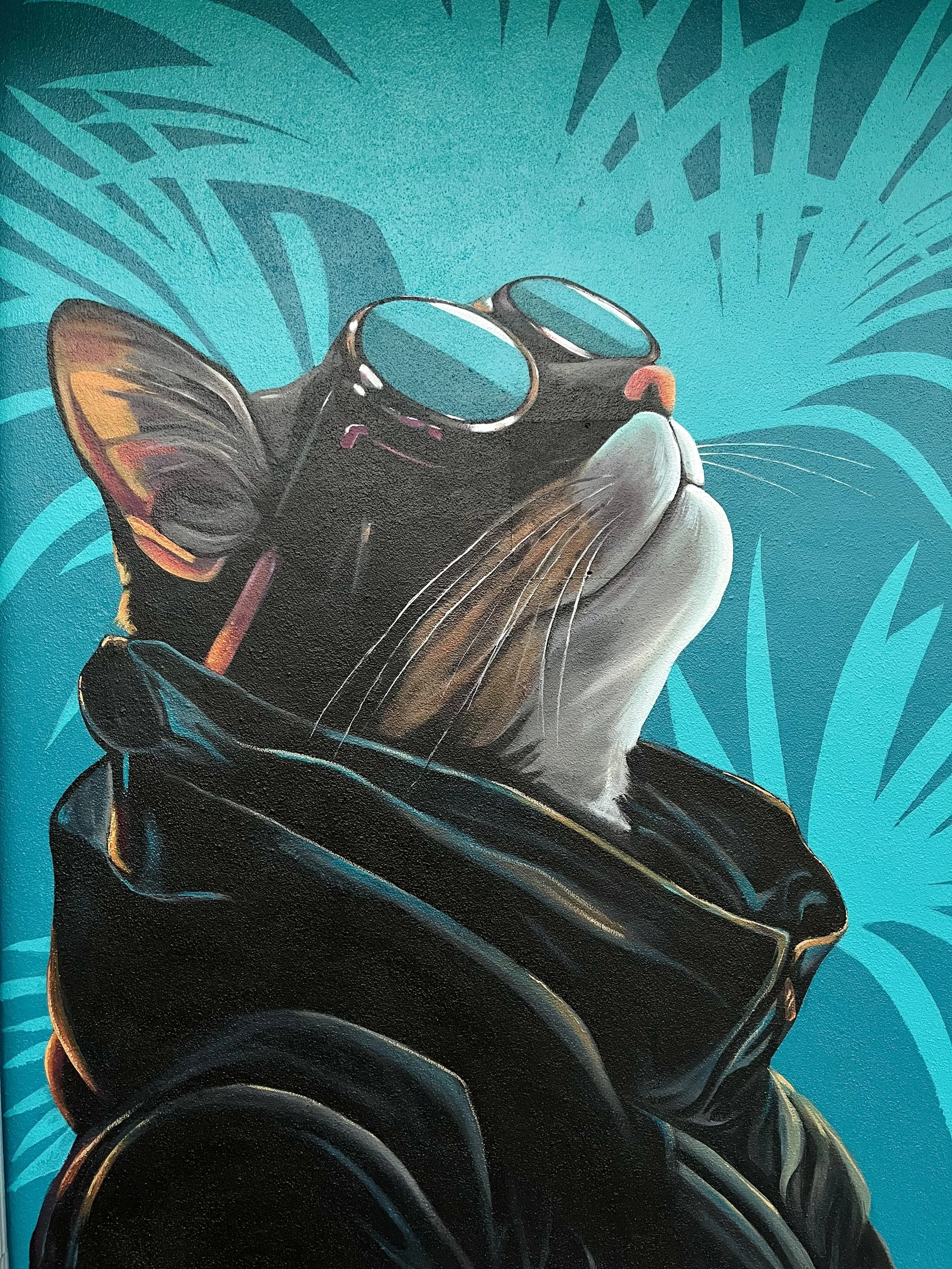 A painting of a cat wearing sunglasses and a black leather jacket, with a turquoise background featuring palm leaves.