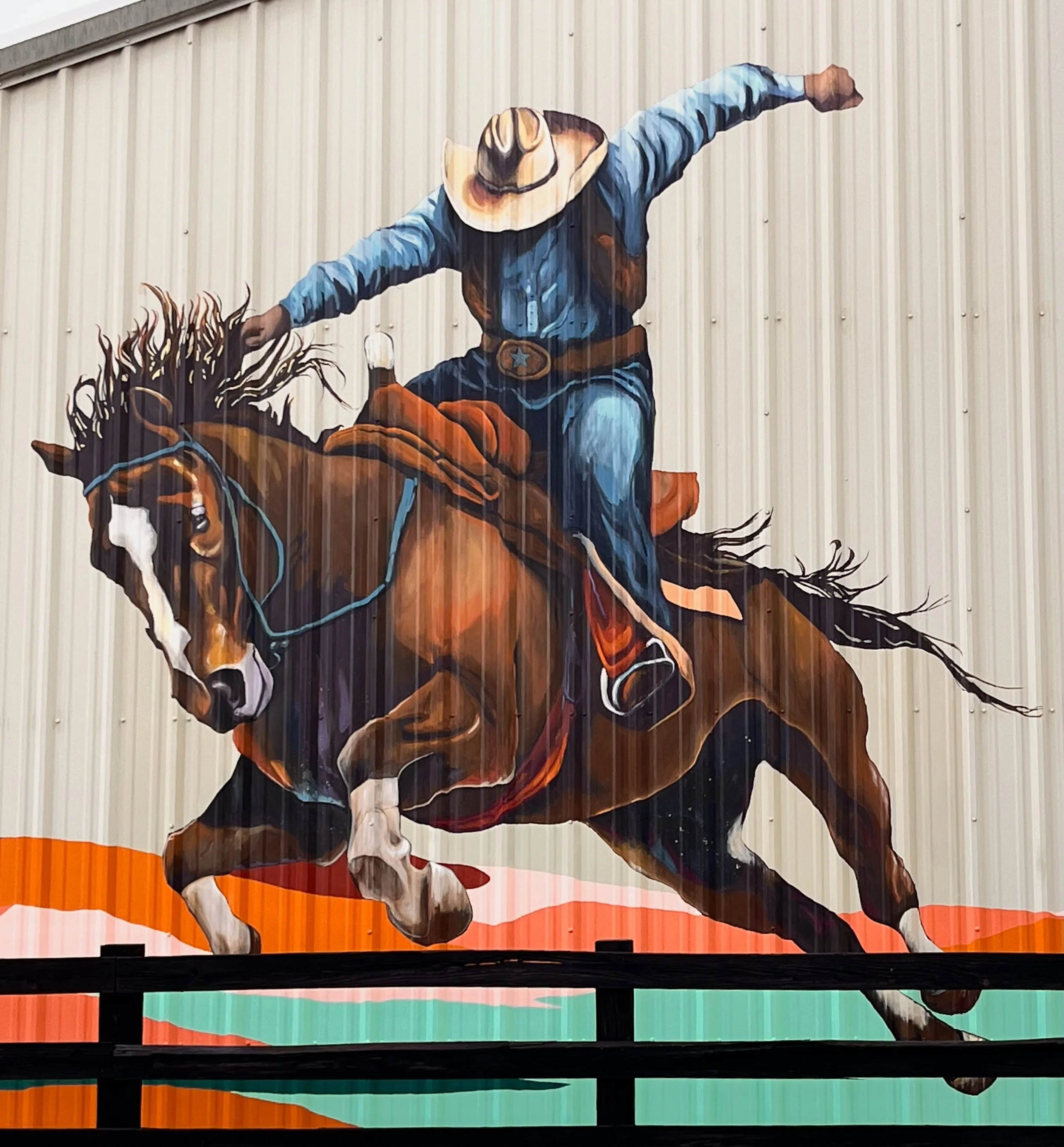 Colorful mural of a cowboy riding a bucking horse, wearing a hat and jeans.