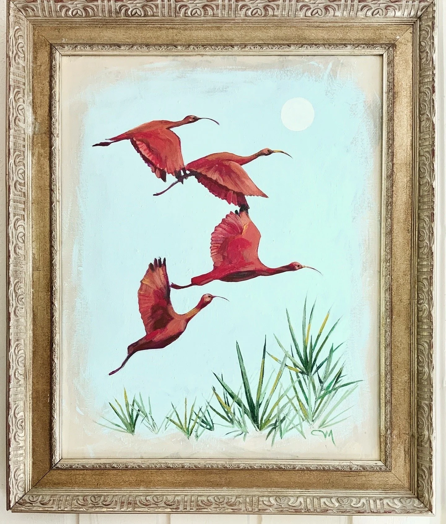 Painting of four red ibises in flight above green grass, with a white moon in a light blue sky, framed in an ornate gold frame.