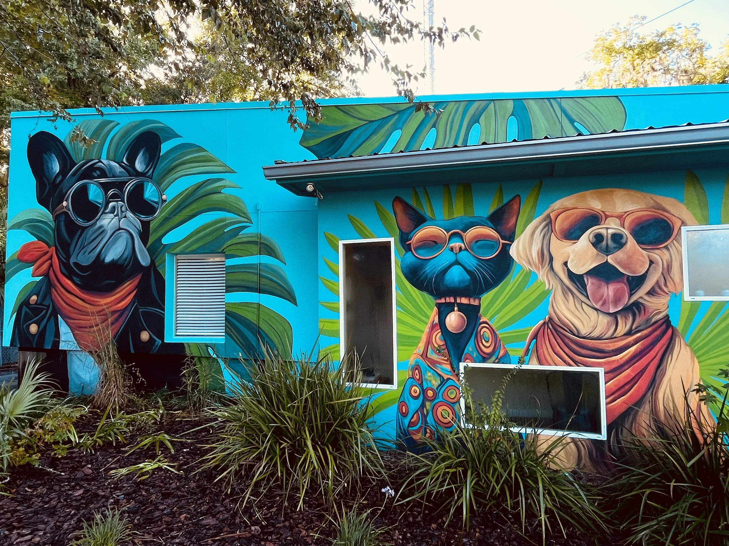Colorful mural of three dogs wearing sunglasses on a blue background with green leaves.