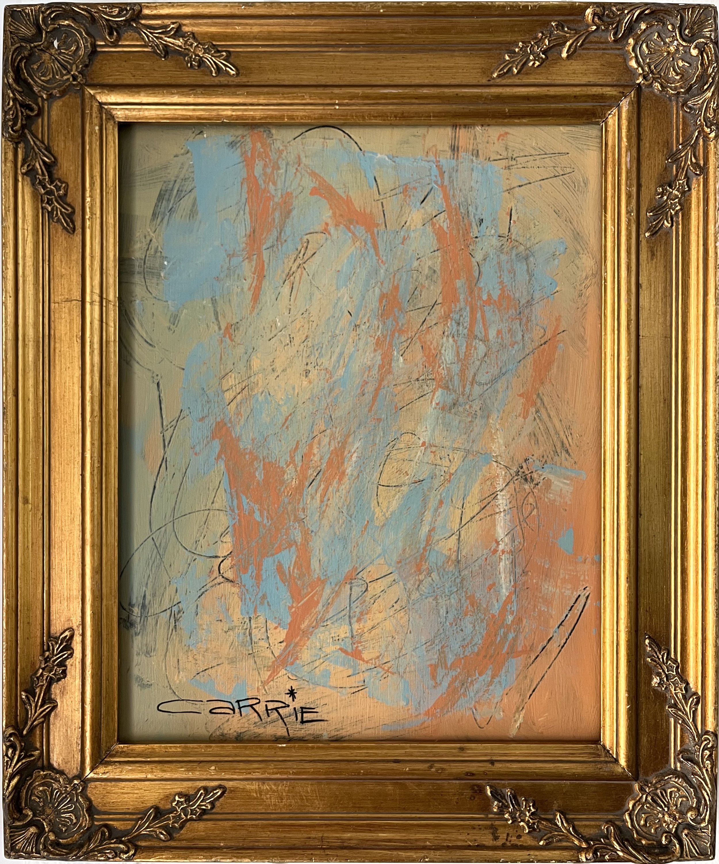Framed abstract painting with splashes of blue, orange, beige, and black paint on a canvas. The frame is ornate and gold-colored with decorative floral patterns in each corner. The bottom left corner of the painting has the word 'SERIE' written in bl