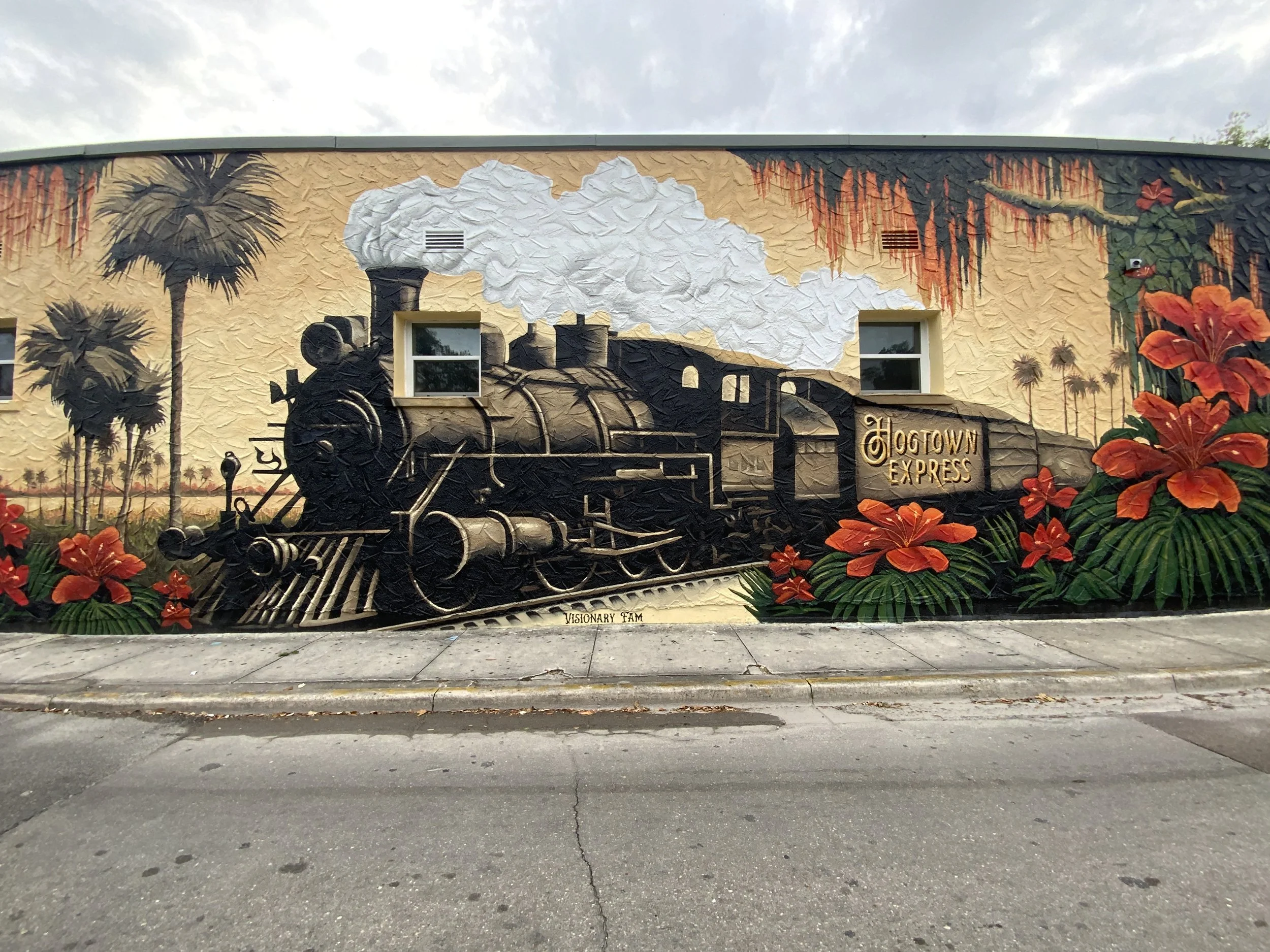 A street mural depicting a steam locomotive train labeled 'Hogtown Express' with red flowers and palm trees on a beige background.