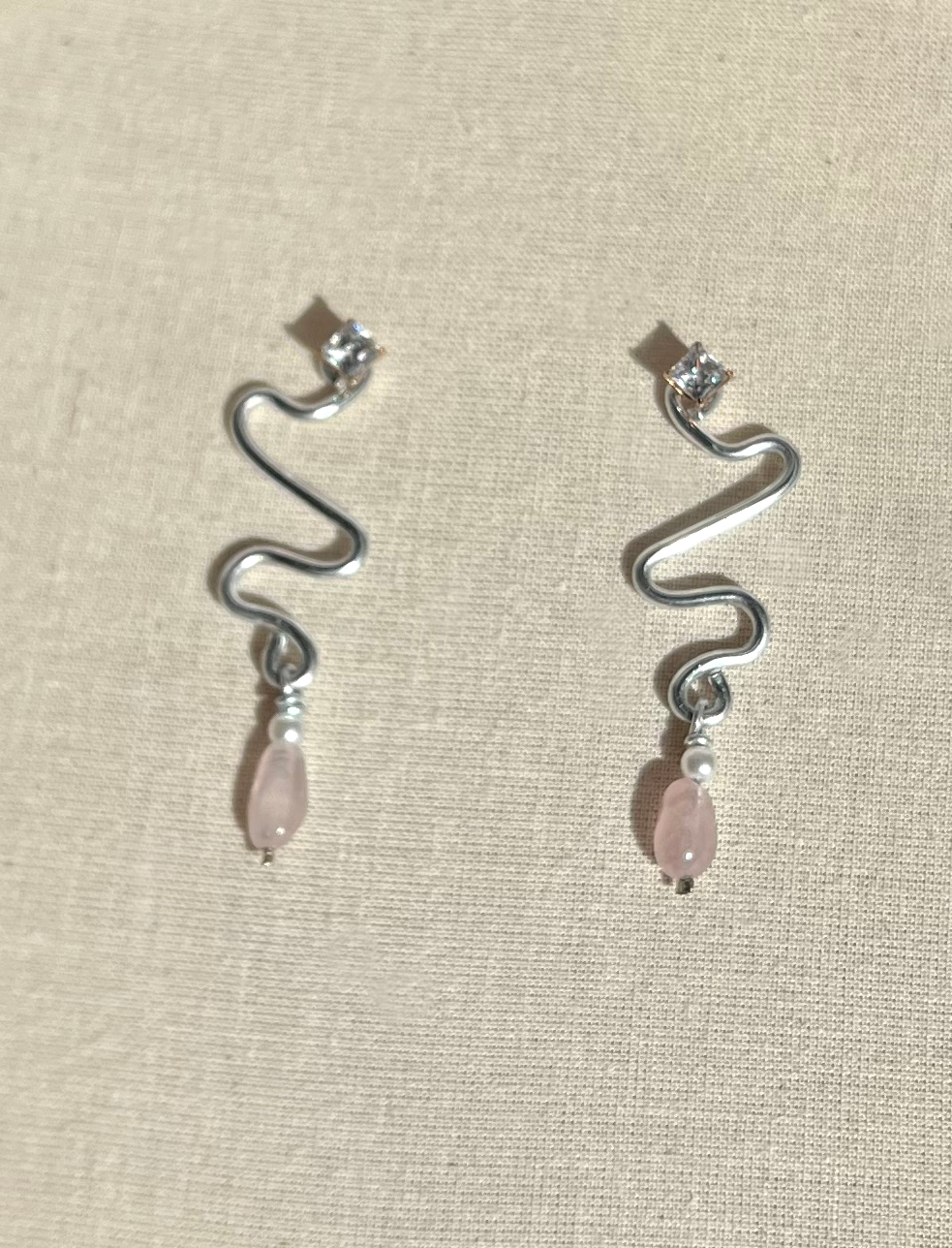 Silver earrings with a curved, wavy design, topped with small sparkling stones, and adorned with pink teardrop-shaped beads and small white pearls.