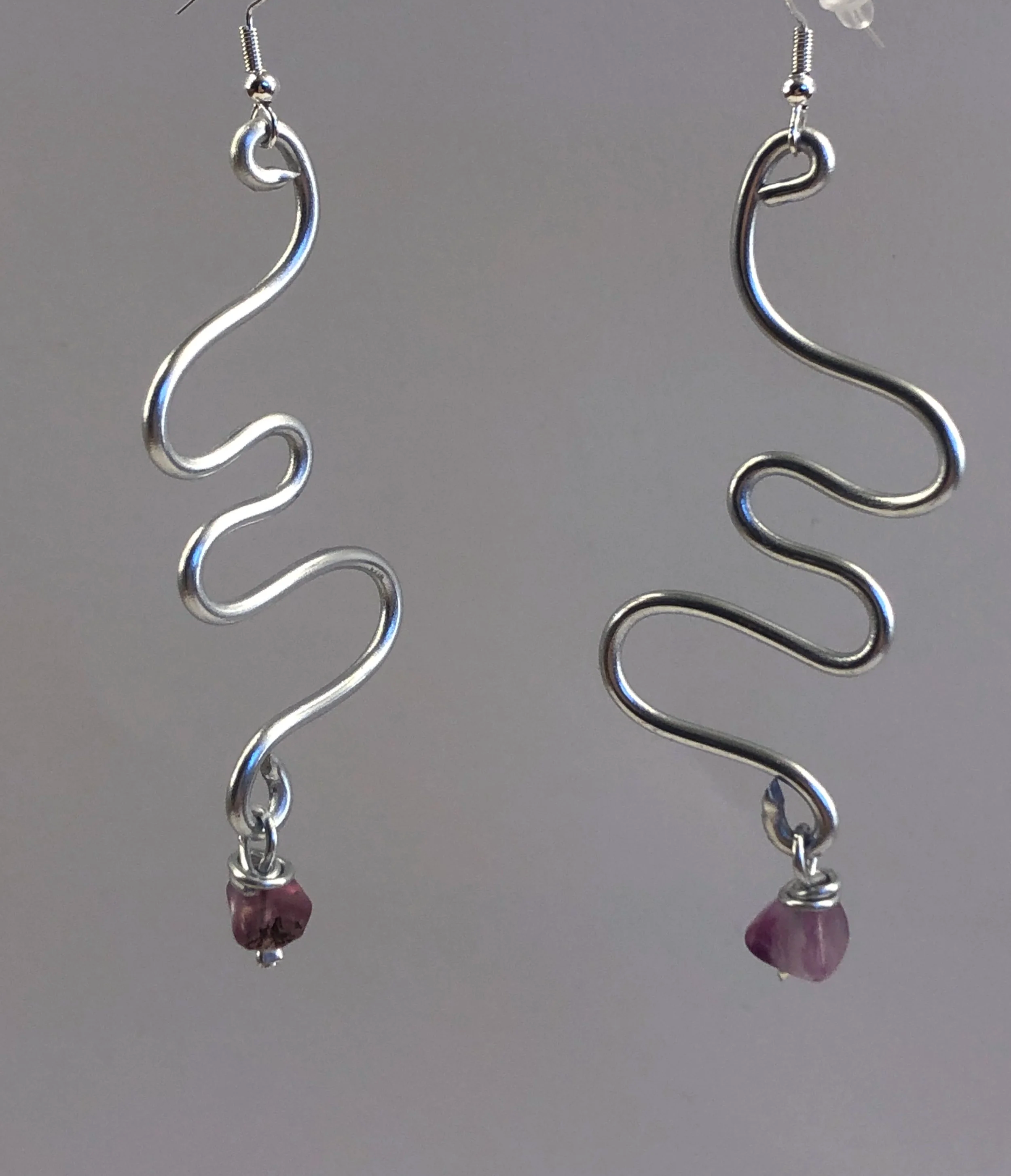 Silver wavy earrings with pink gemstone dangles against a gray background.