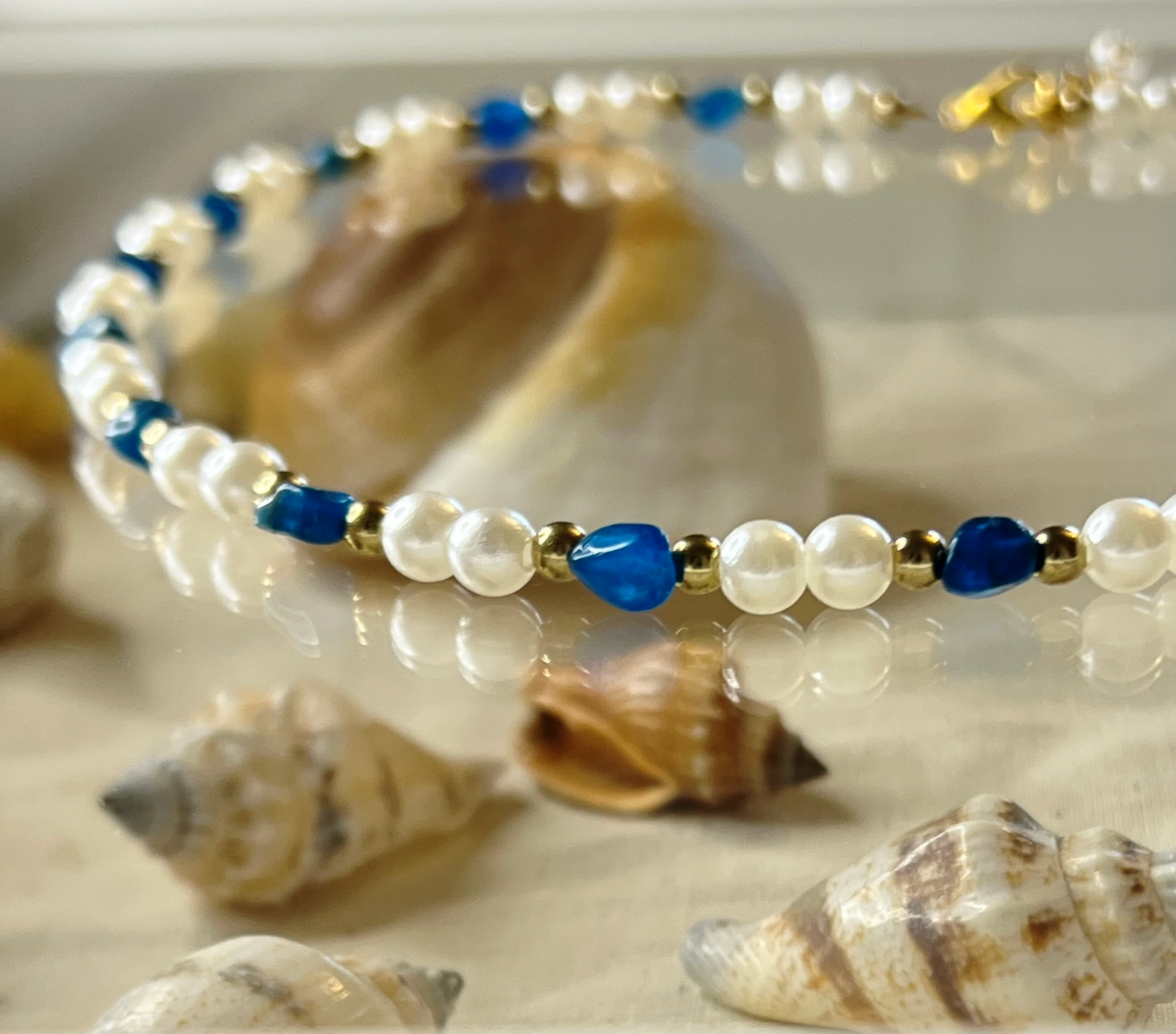 A pearl and blue bead necklace surrounded by seashells on a light surface.