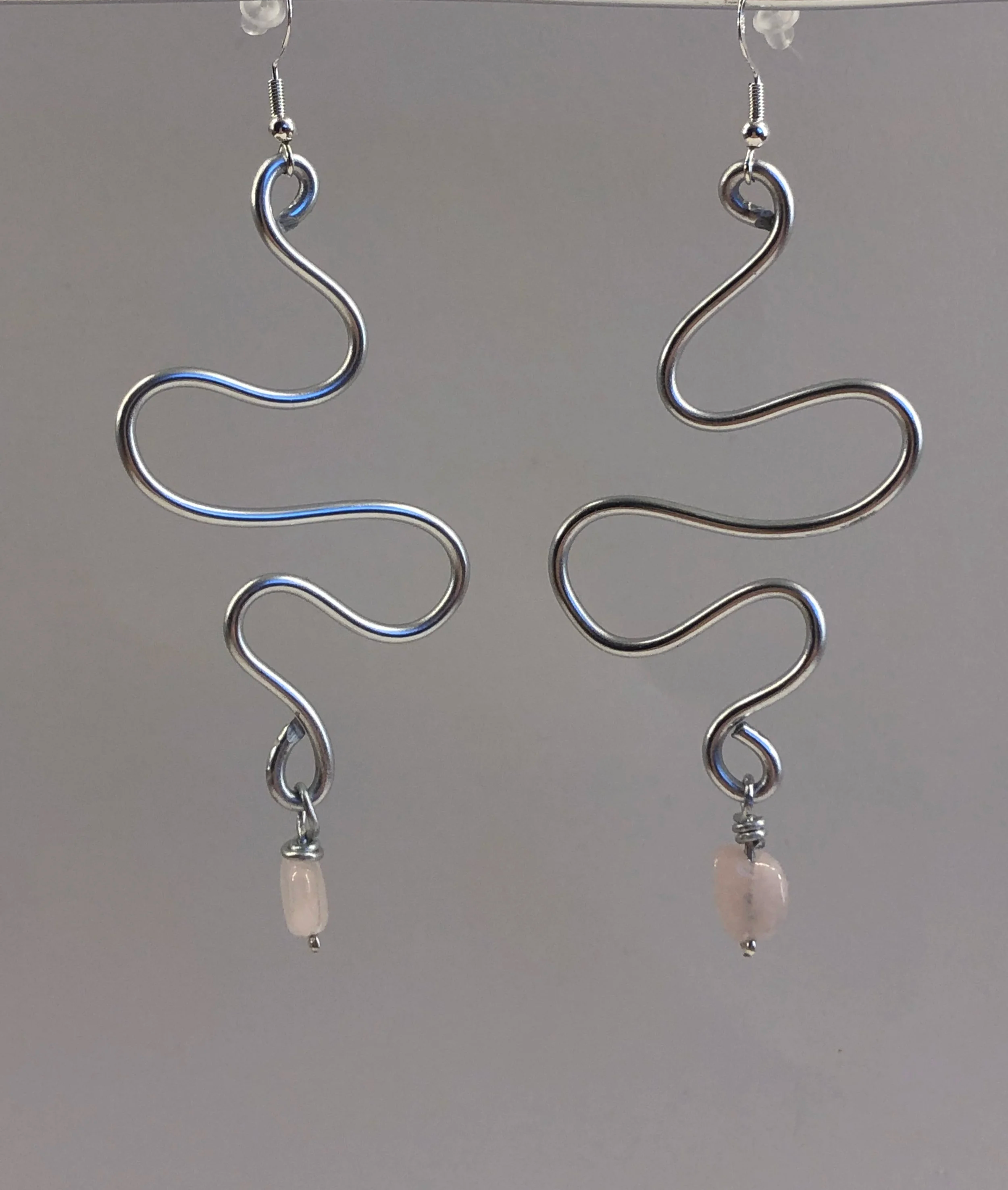 Silver wavy earrings with small pink beads at the bottom, hanging from hooks.