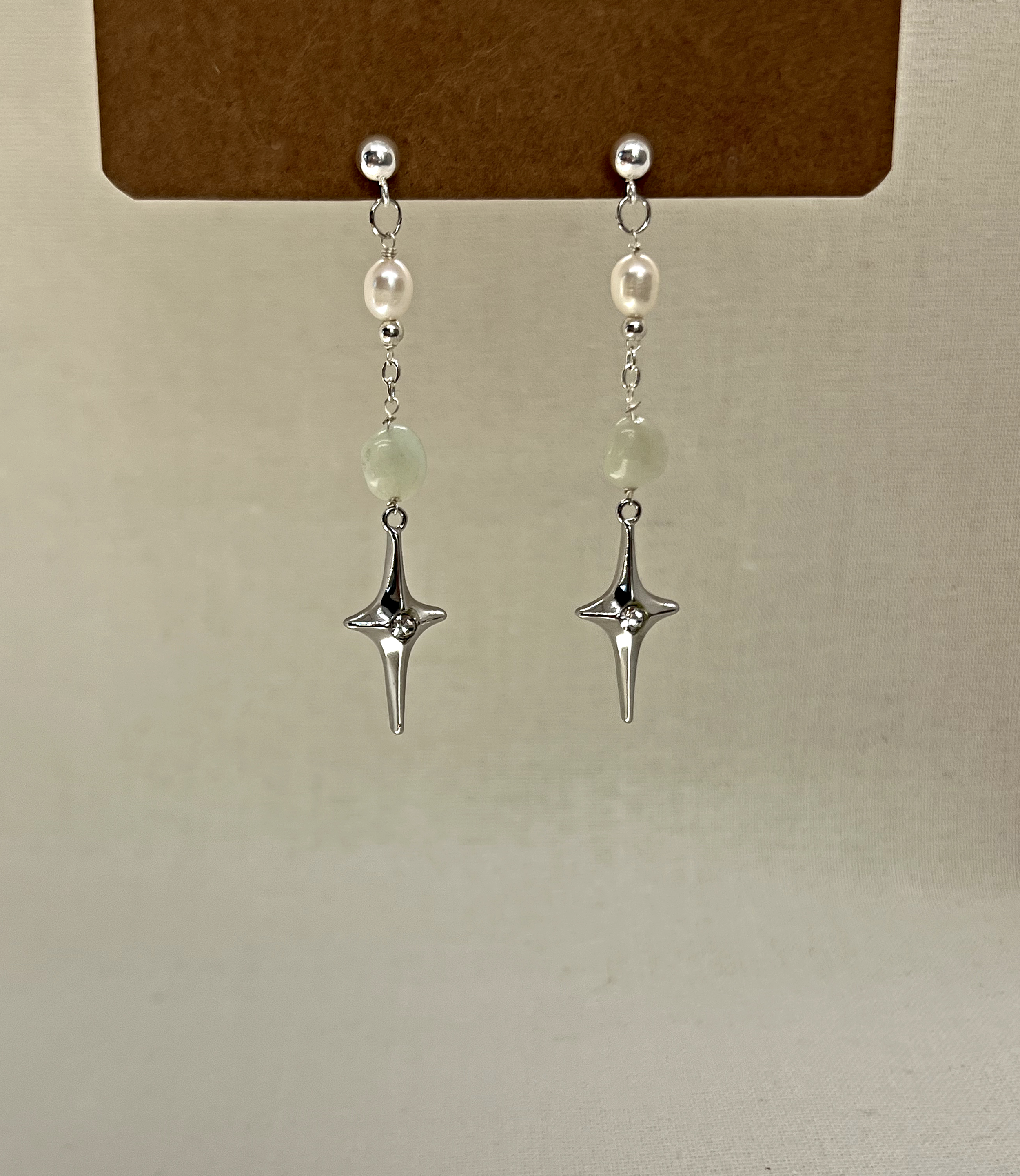 Silver dangle earrings with white pearls, light green beads, and star-shaped charms hanging from silver chains.