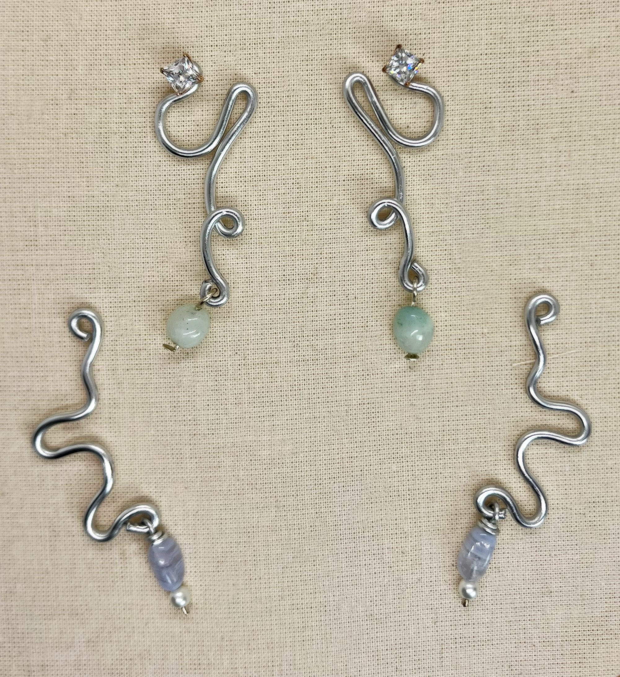 Silver wavy earrings with beads at the end, displayed on beige fabric