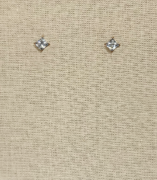 A pair of small diamond stud earrings on beige fabric background.