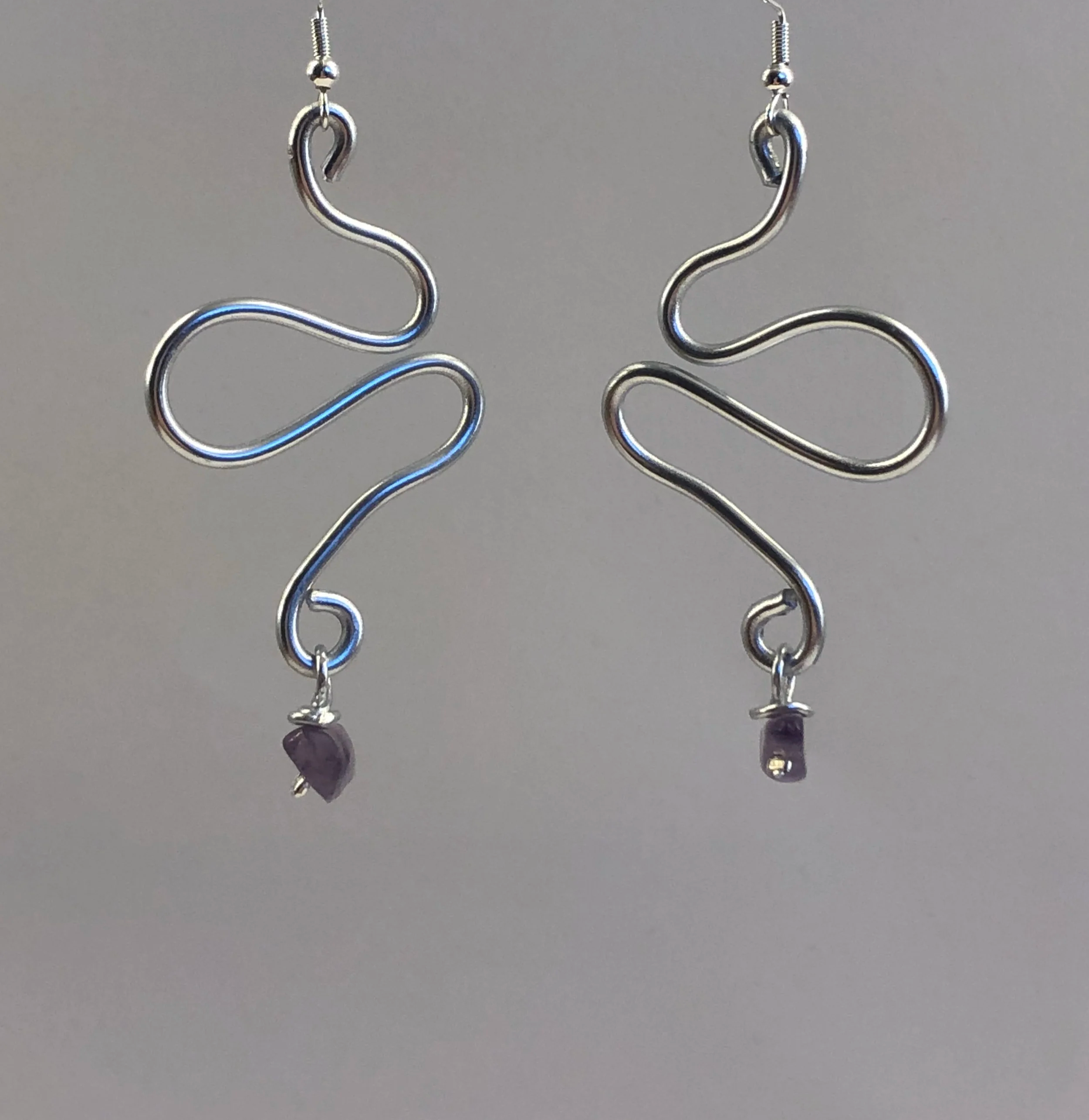 Silver earrings with a wavy, S-shape design and a small purple stone at the bottom.