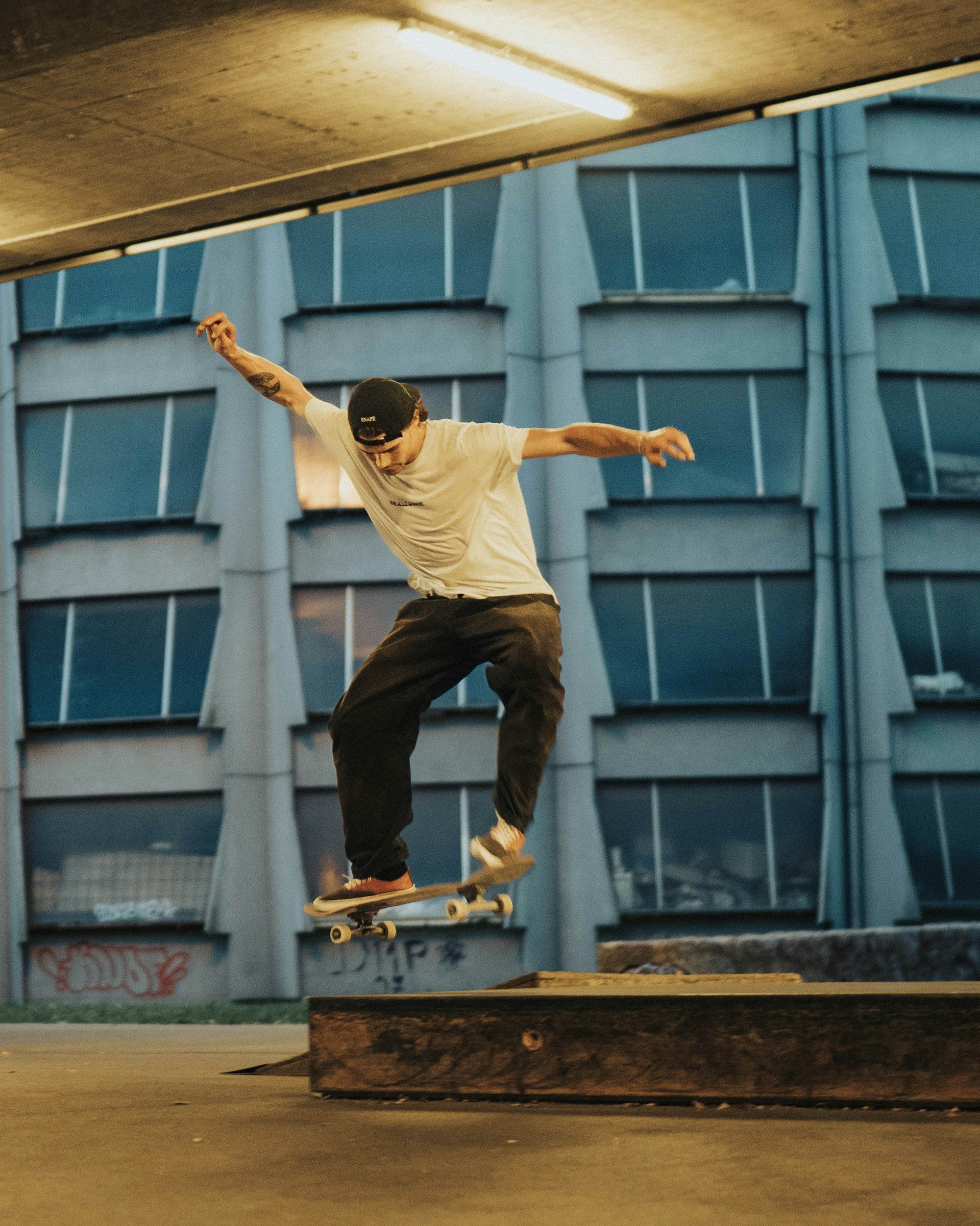 A skateboarder performing a trick on a ledge in an urban skate park with modern building in the background.