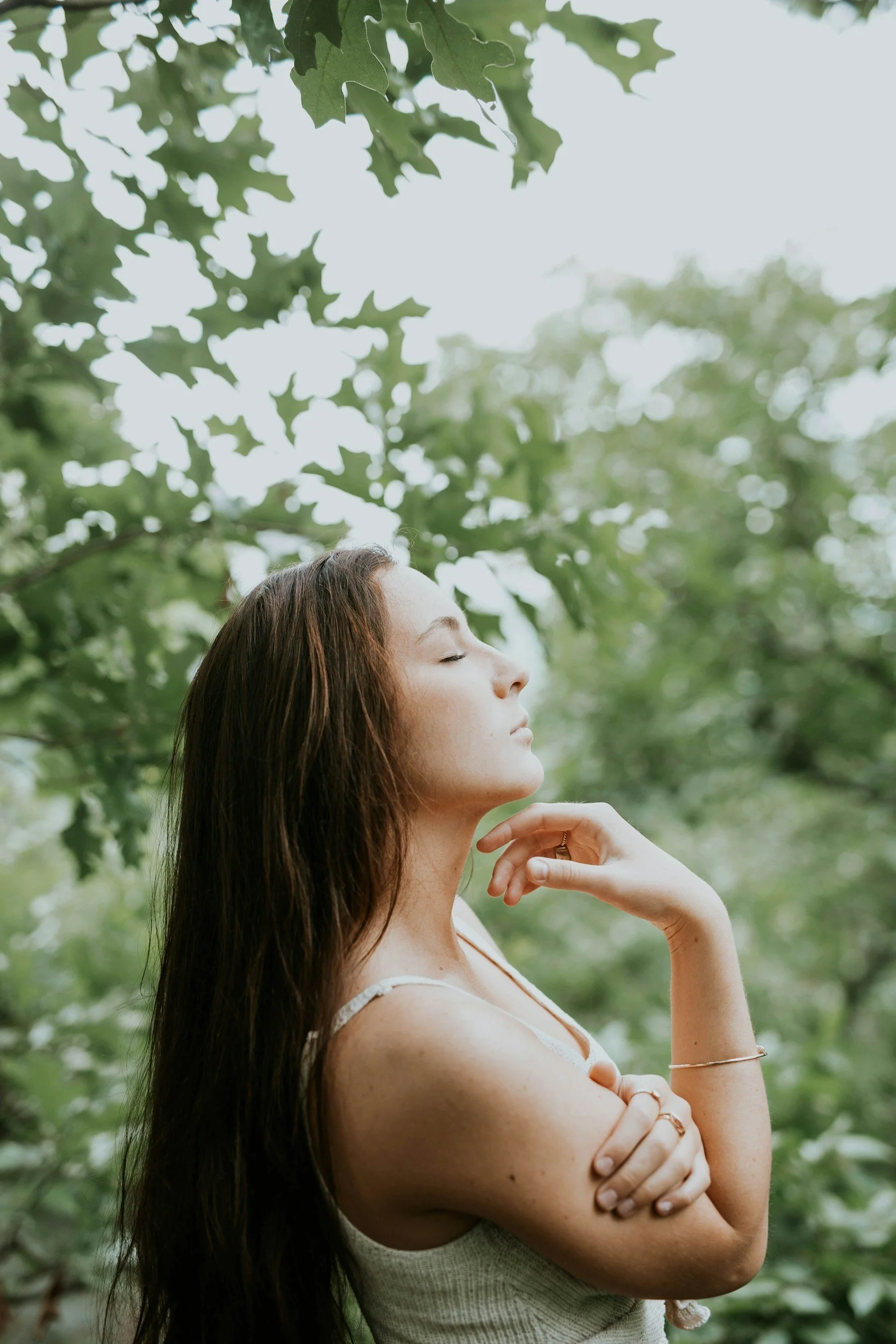 Profile of a woman with closed eyes and relaxed expression, outdoors surrounded by greenery.