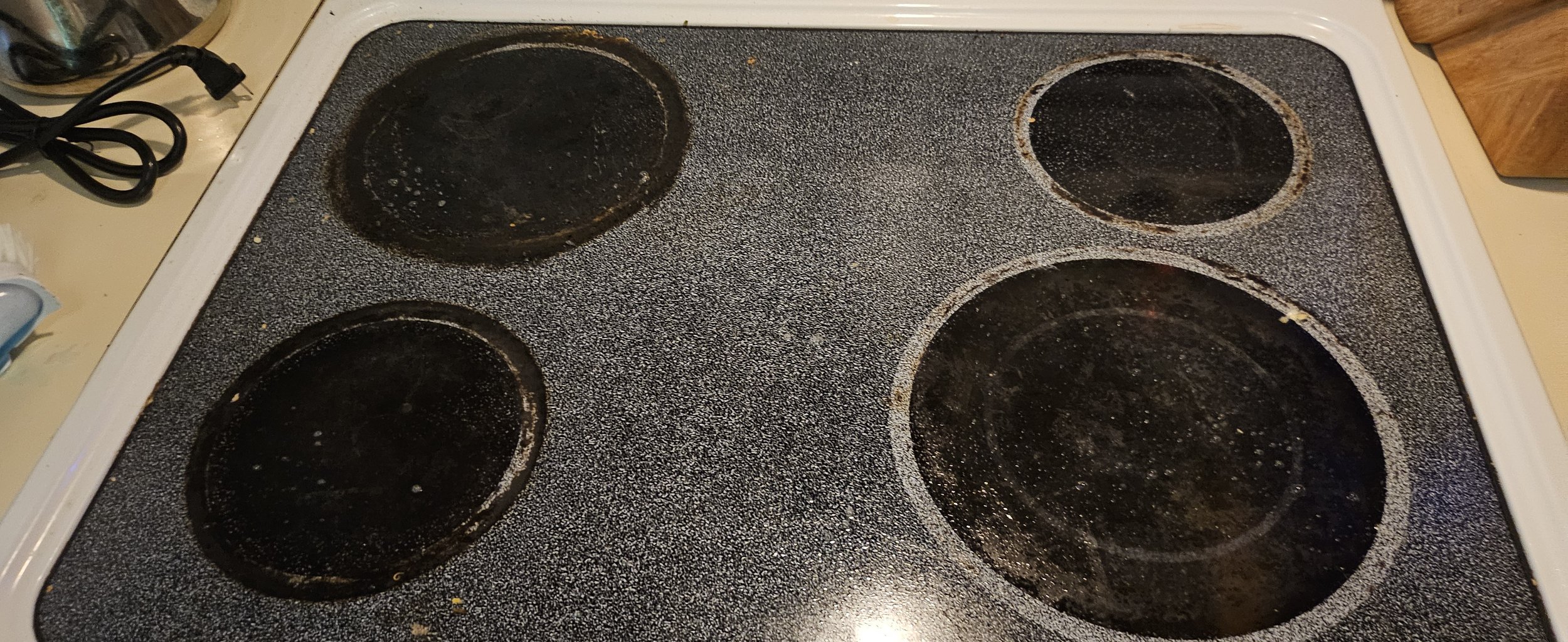 Dirty and stained electric stovetop with five burnt and greasy burners.