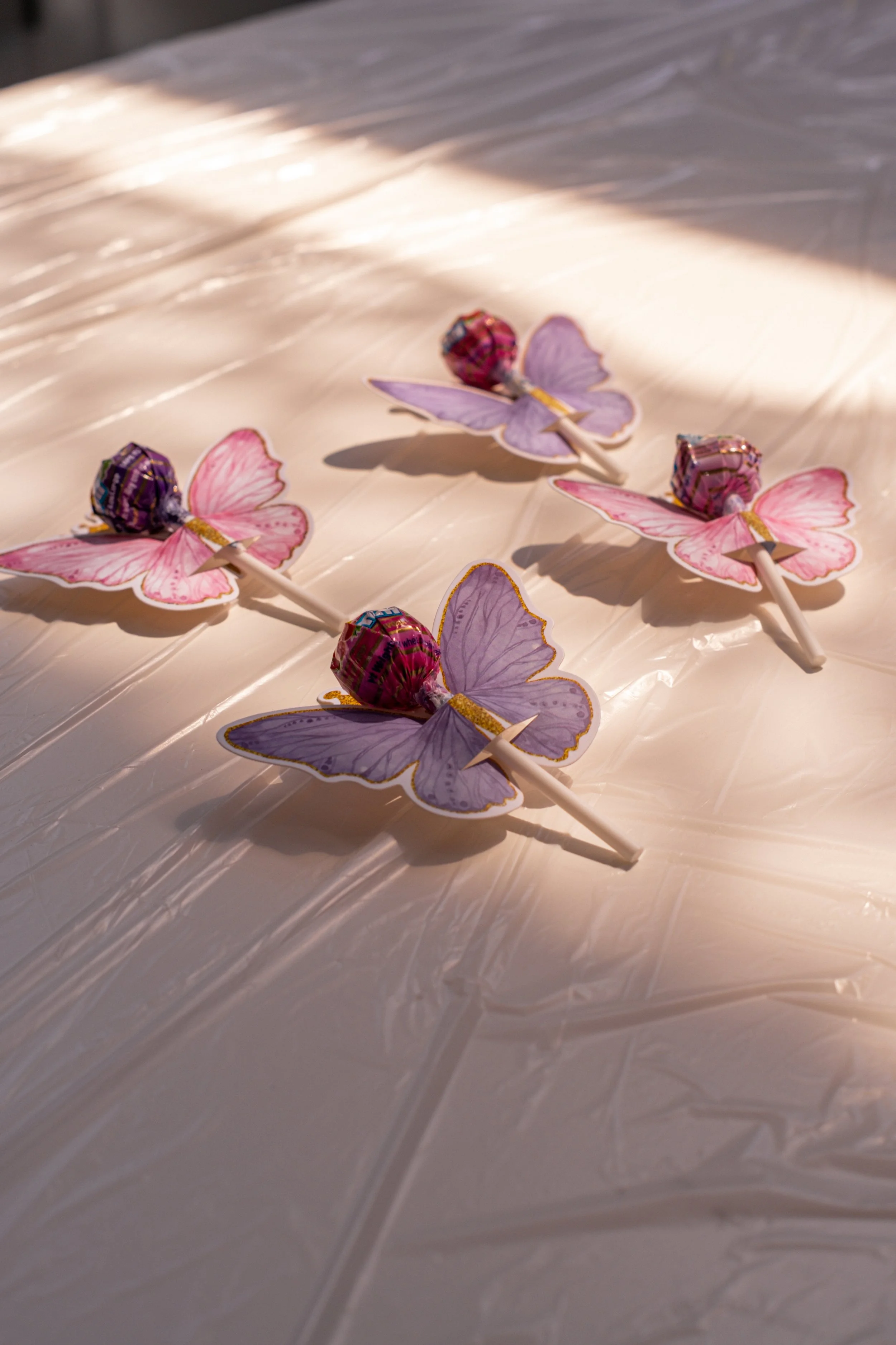 Decorative butterfly-shaped lollipops with purple and pink wings on a shiny, crinkled white surface.